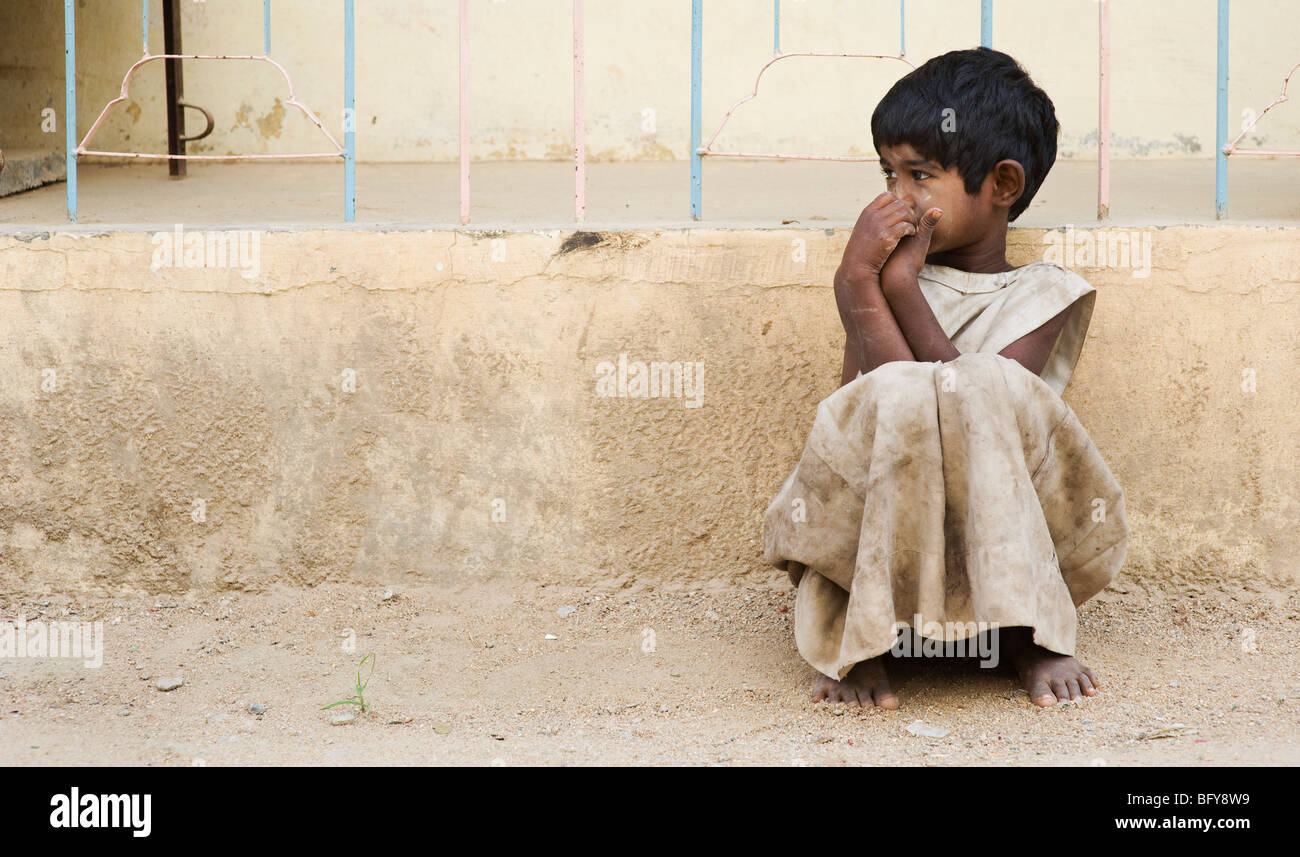 Young poor Indian girl leaning against a wall, alone on the street, in rural  India with copy space Stock Photo