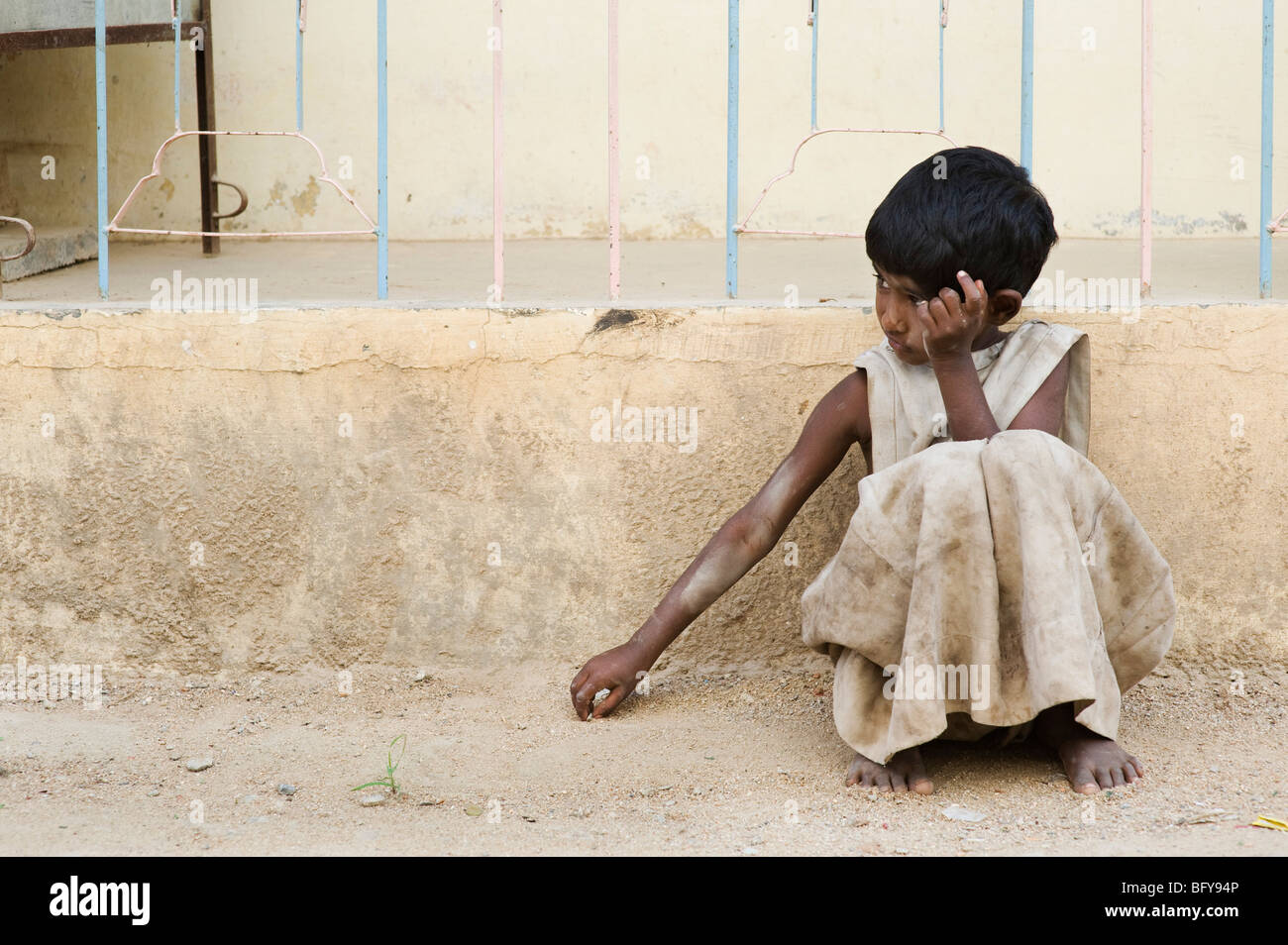 Young poor Indian girl leaning against a wall, alone on the street, in rural  India with copy space Stock Photo