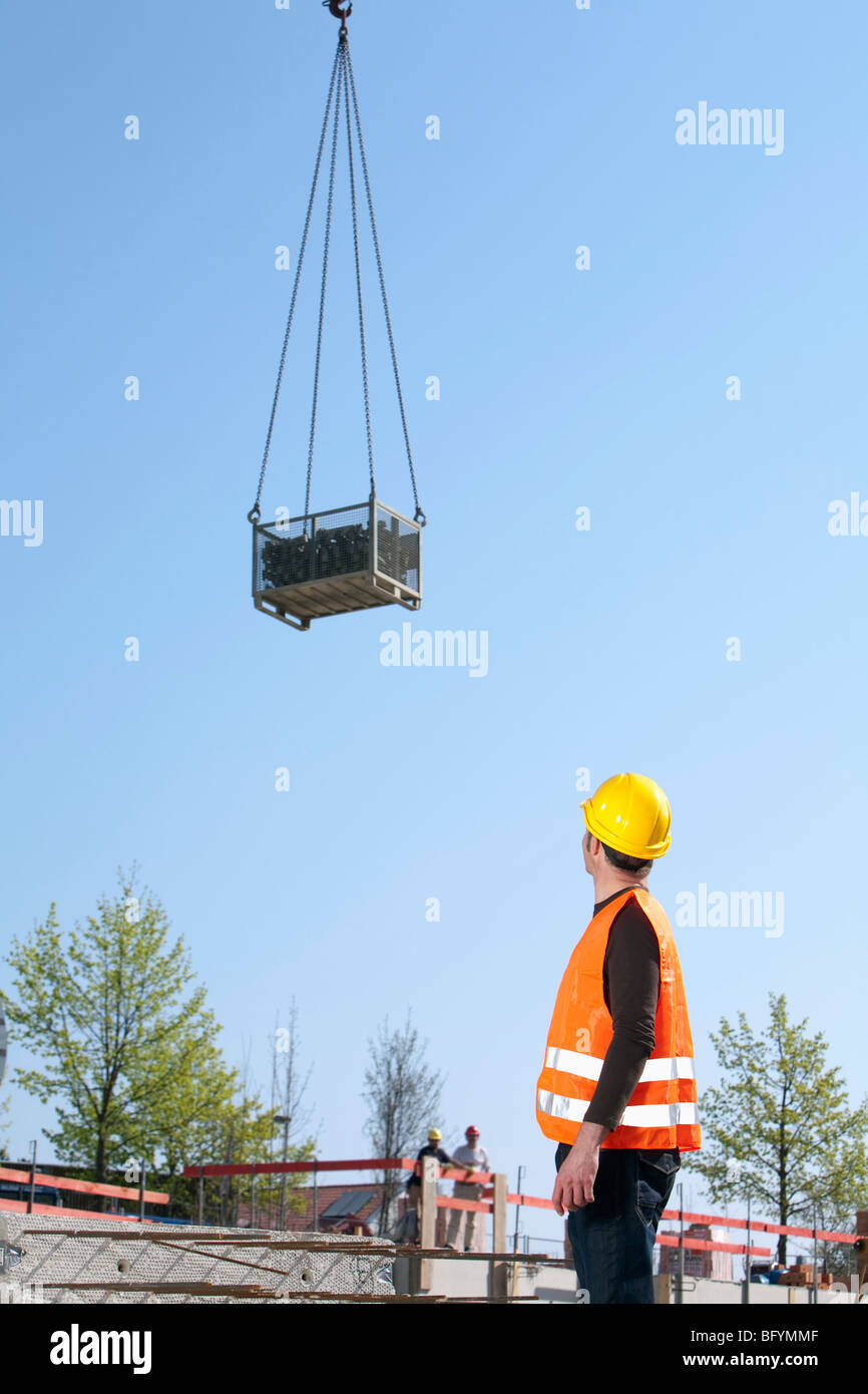 construction worker watching load being lifted by tower crane Stock