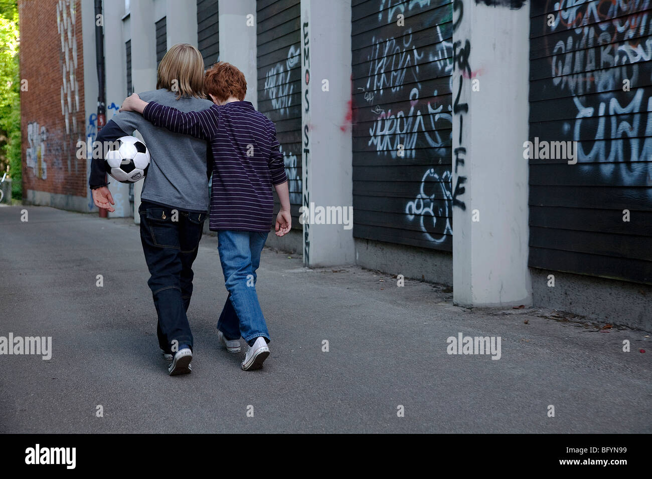 rear view of two young boys walking together through street with football Stock Photo