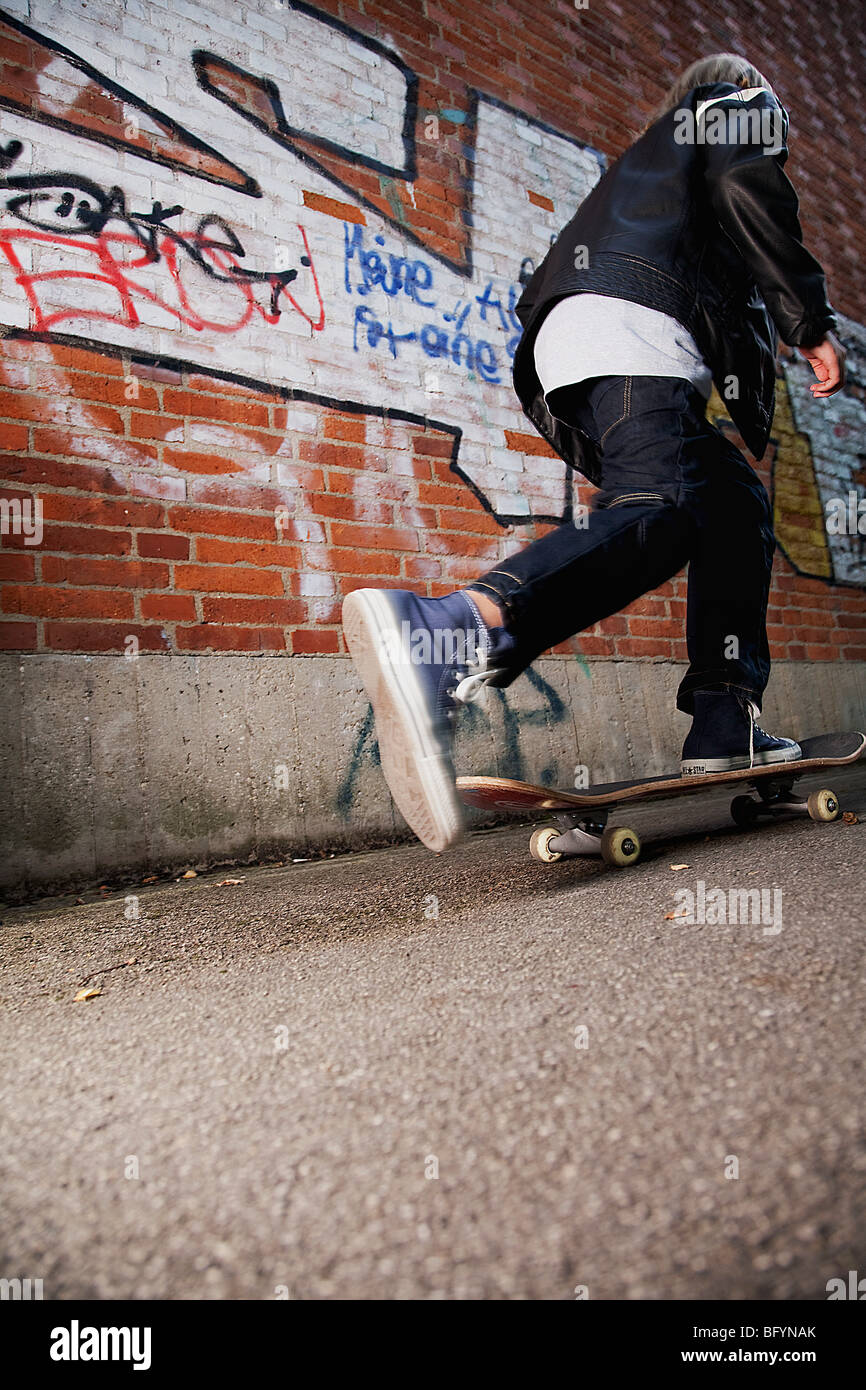 rear view of young boy skateboarding along wall Stock Photo