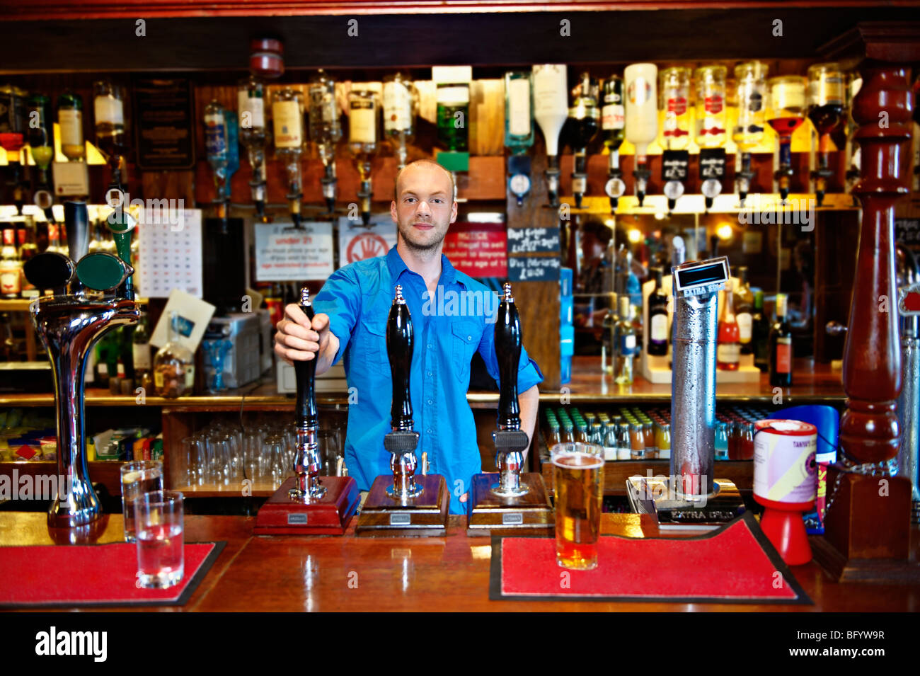 Barman standing behind bar in pub Stock Photo
