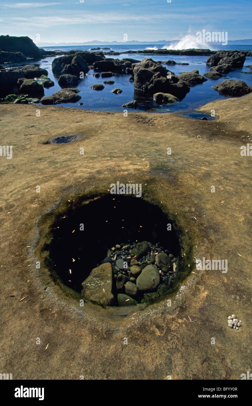 Distinctive round hole in tide pool, wave splash, rocky coast Stock