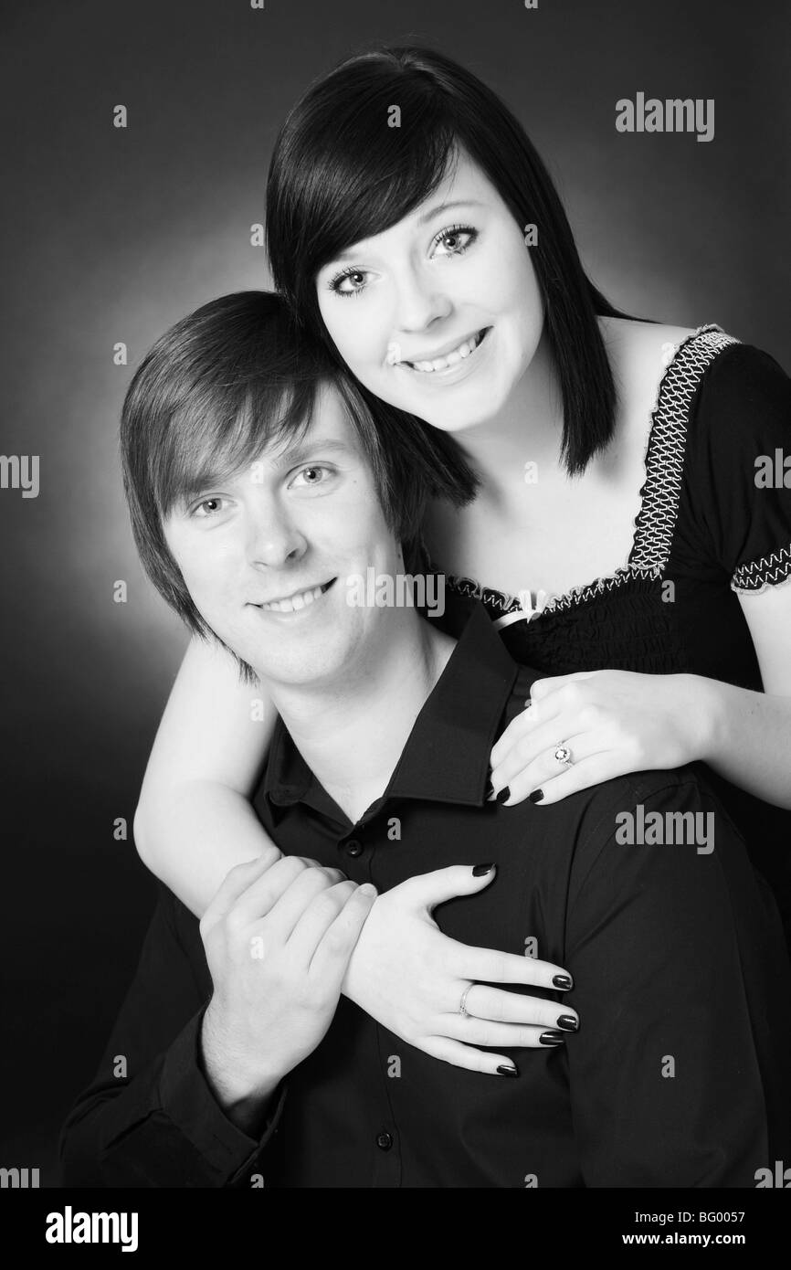 A black and white photograph of an attractive young white couple hugging and smiling in a photographic studio setting Stock Photo