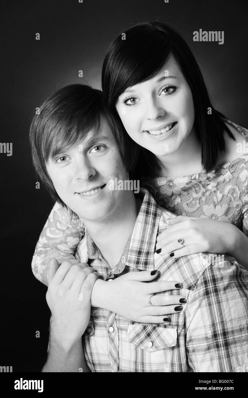 A black and white photograph of an attractive young white couple hugging and smiling in a photographic studio setting Stock Photo