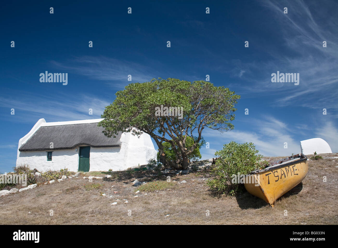 Thatched roof white washed cottage in Struisbaai, SA with boat at