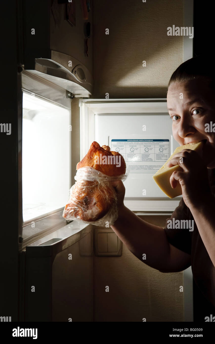 woman in front of the fridge eating cheese Stock Photo