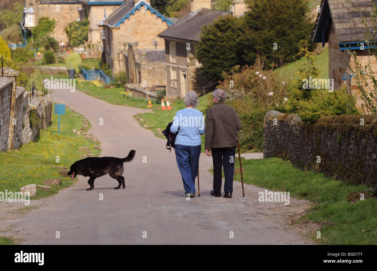 Elderly couple walking down the main road in Edensor Village Chatsworth Park Derbyshire Stock Photo