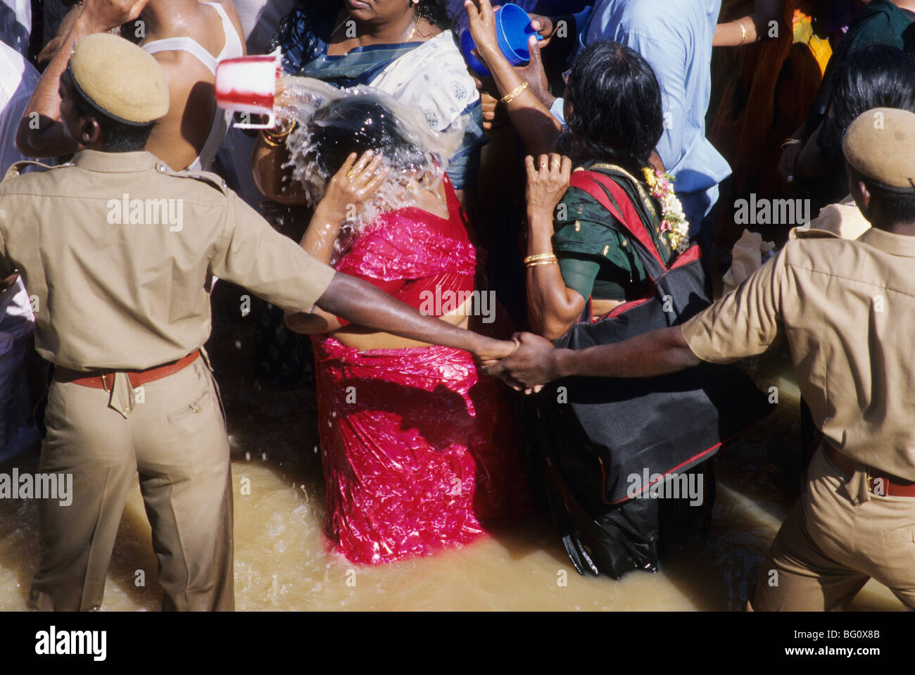 Policemen are keeping order as pilgrims and devotees take a holy dip and splash water on one another in the Mahamaham temple tank during the Hindu Kumb Mela festival that is celebrated every 12 years in a small temple-town called Kumbakonam in the state of Tamil Nadu, India. It is believed that taking a bath or sprinkling water of the tank on their bodies will cleanse them of all their sins. This festival, called the Mahamaham festival, took place in March of 2004. Stock Photo