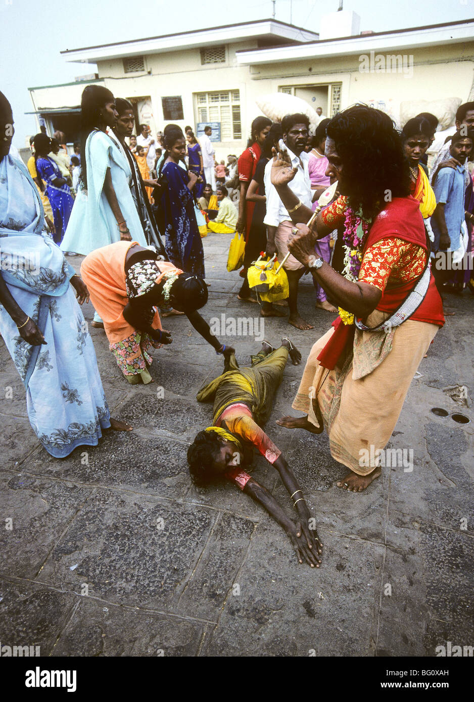 A pilgrim rolls on the ground which is hard pavement completely around the Palani Murugan Temple holding a coconut during the annual Hindu Thaipusam festival. She is assisted by family members and a female saddhu who occasionally give her water. This is a form of kavadi which is an act of devotion represented by the hardship and pain she is experiencing. Stock Photo