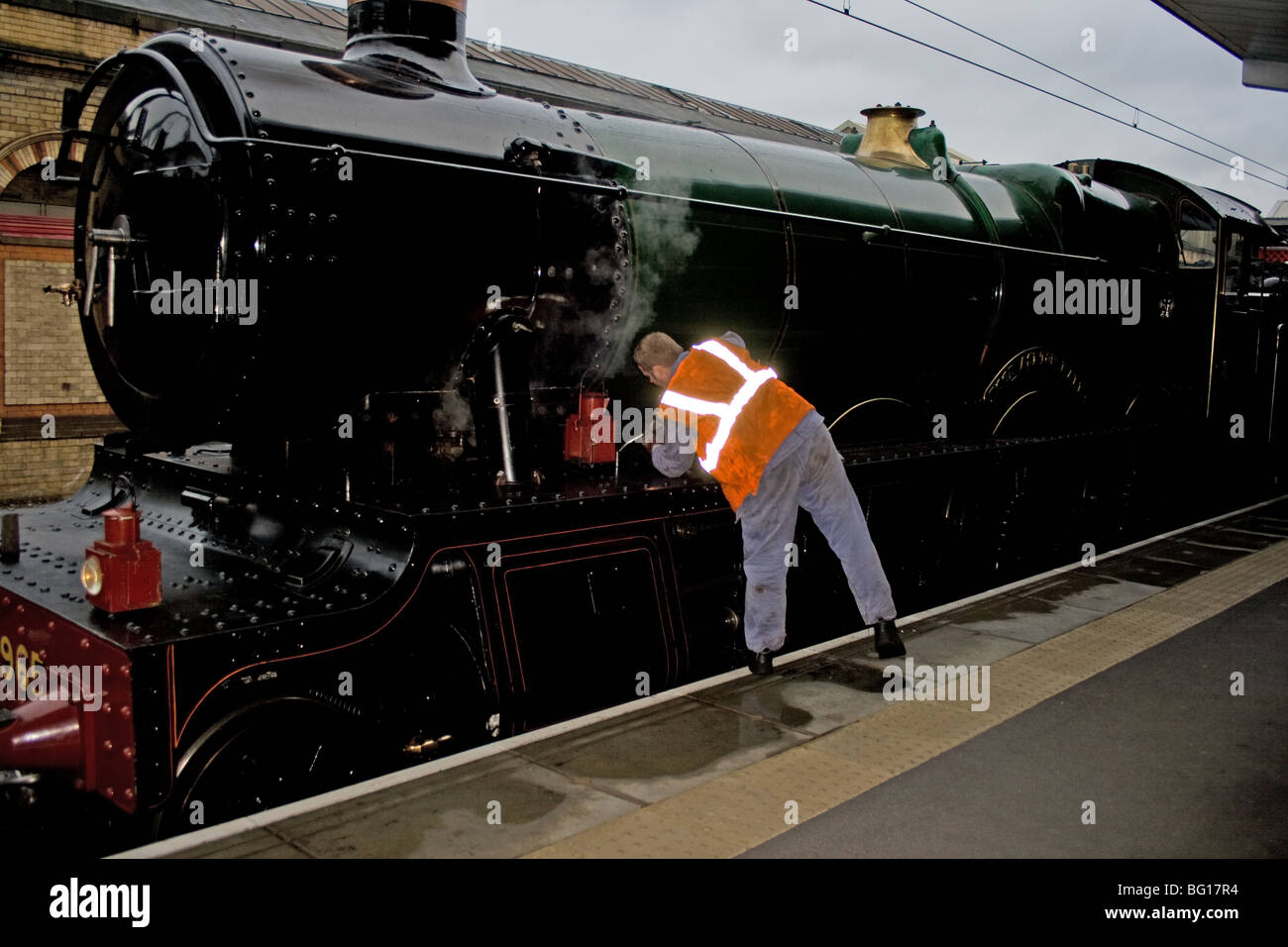 Engine fireman oiling his steam locomotive whilst waiting at a station Stock Photo
