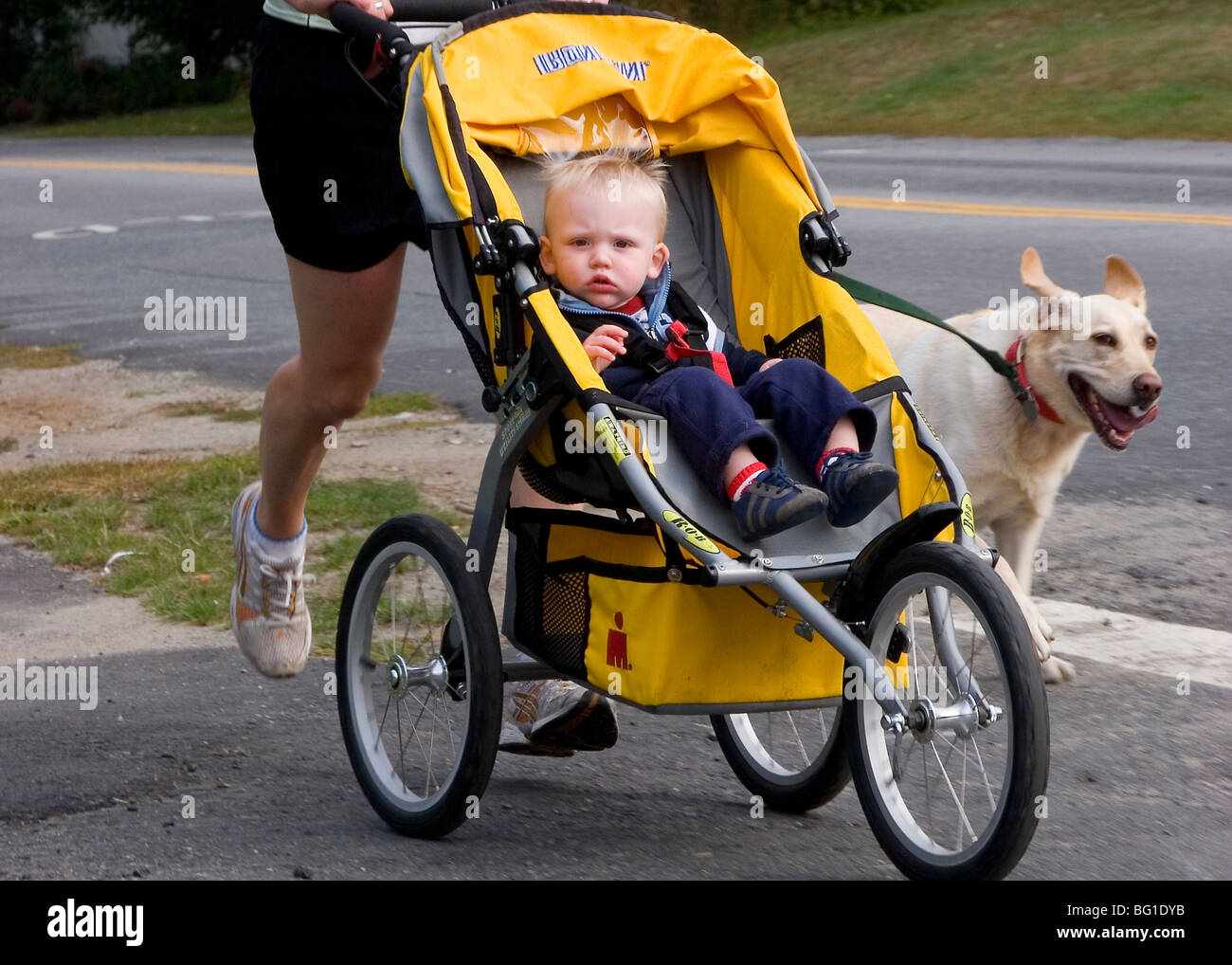 Woman running with dog on leash and child in stroller Stock Photo