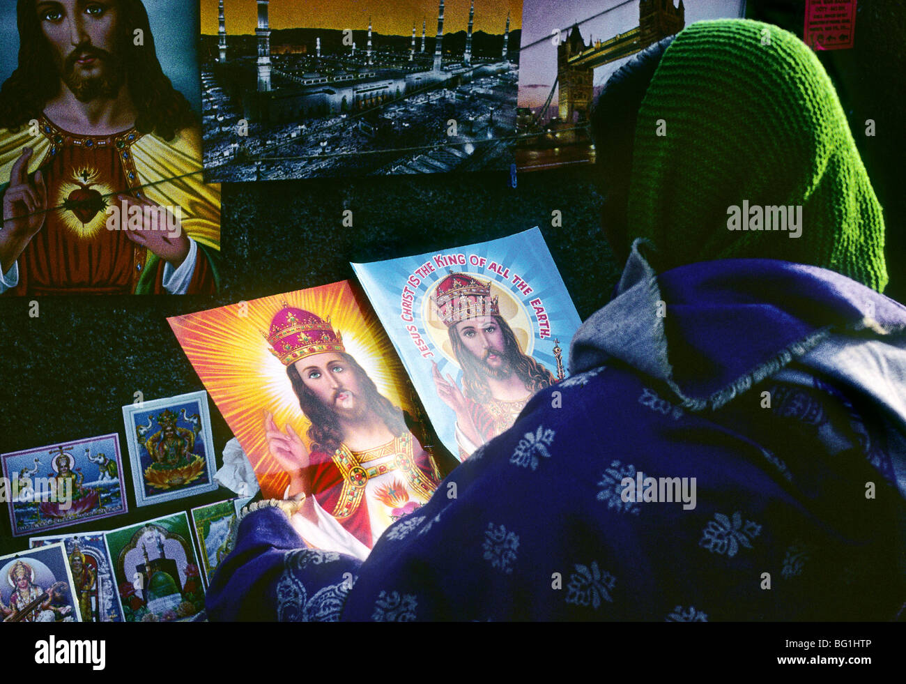 A woman is purchasing small poster-sized images of Jesus at a shop selling Hindu as well as Christian imagery in the public market in Ooty, India Stock Photo