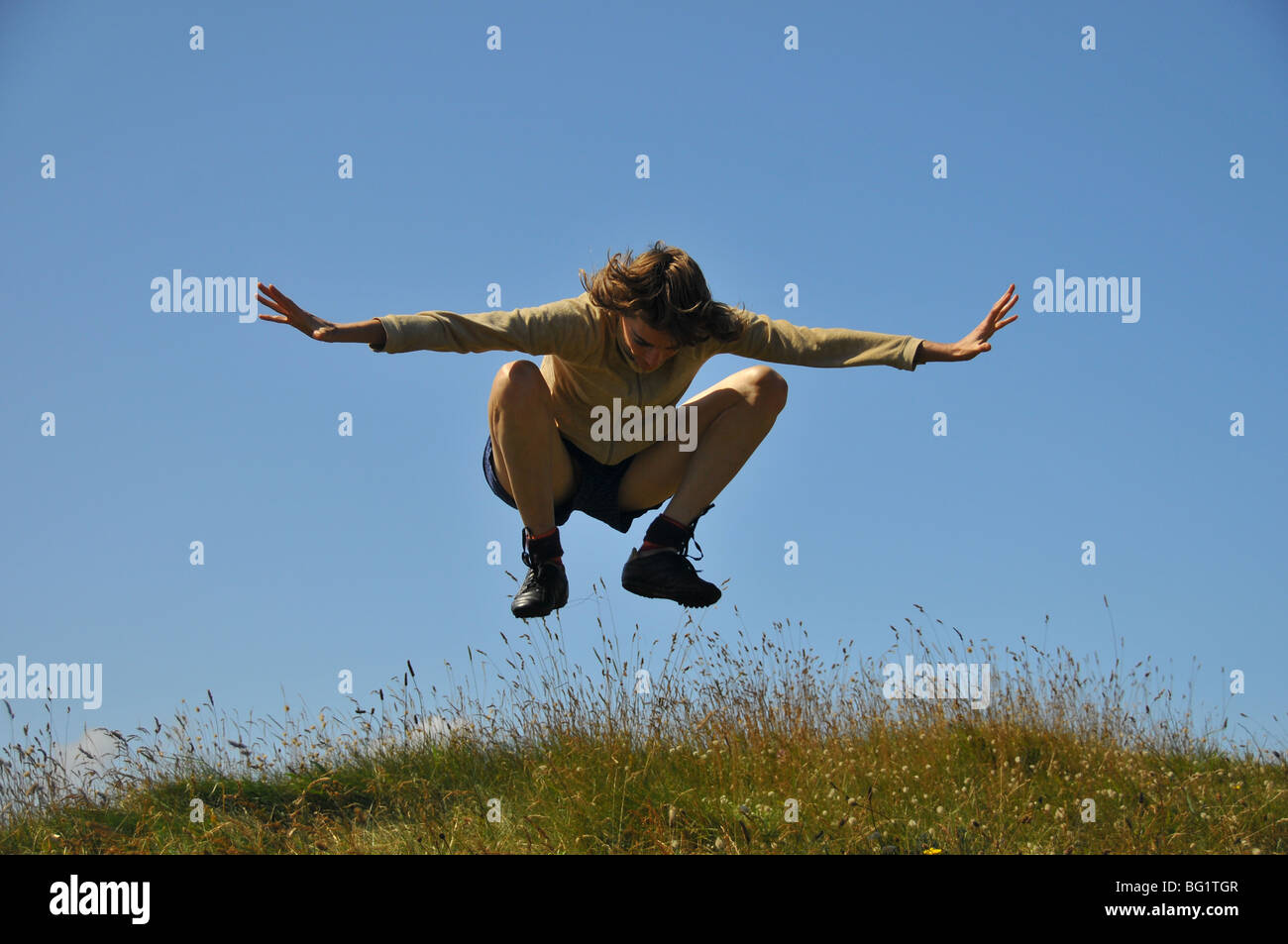 young white woman jumping and leaping on the dune arms up and legs in air and knees bent body in space above ground Stock Photo