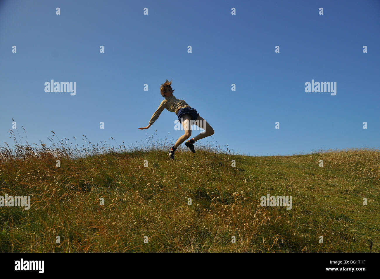 young white woman jumping and leaping on the dune  legs  in air and knees bent imbalance unbalanced body in space above ground Stock Photo