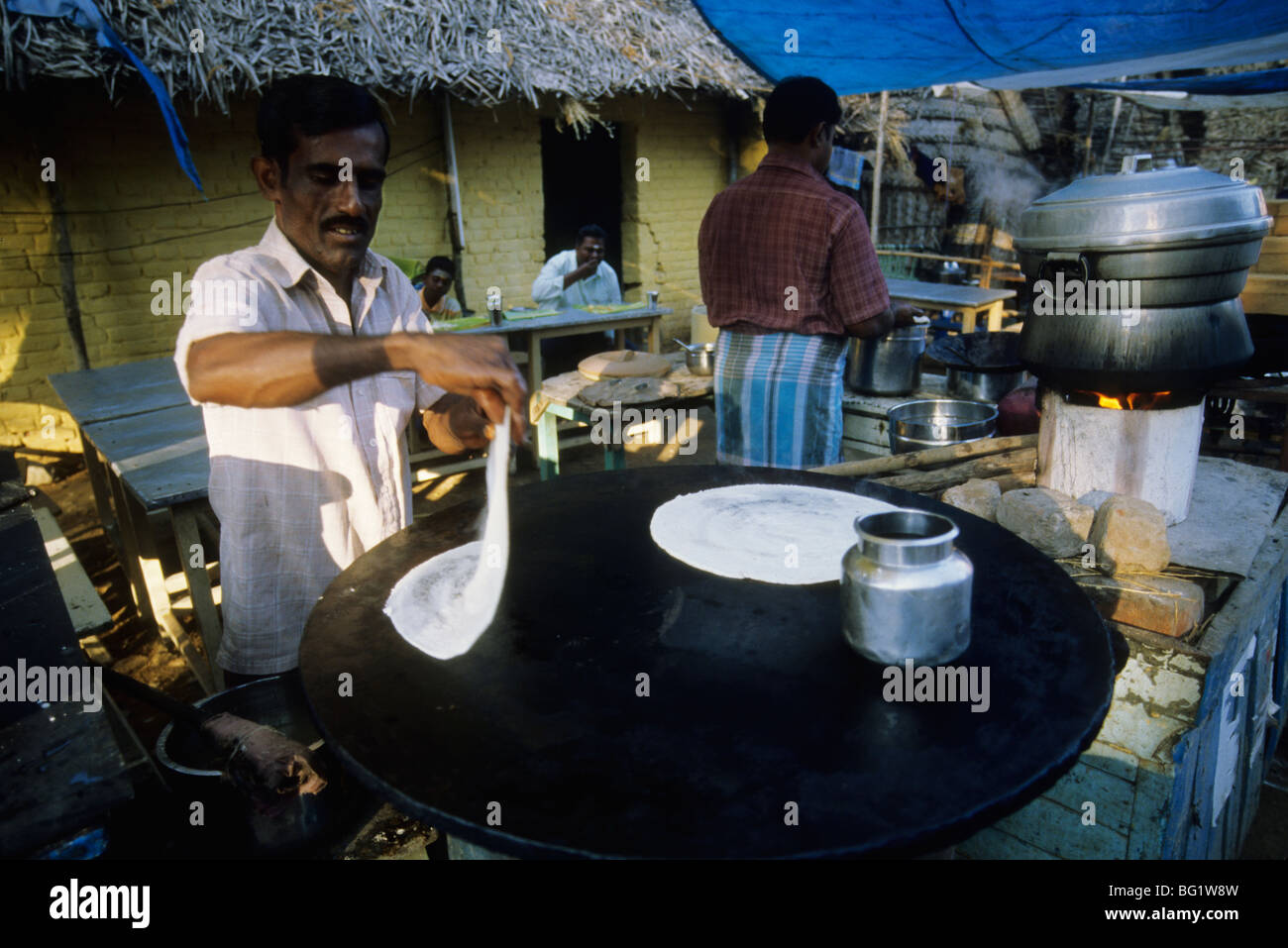 A man makes an Indian unleavened flat bread over a hot griddle in an