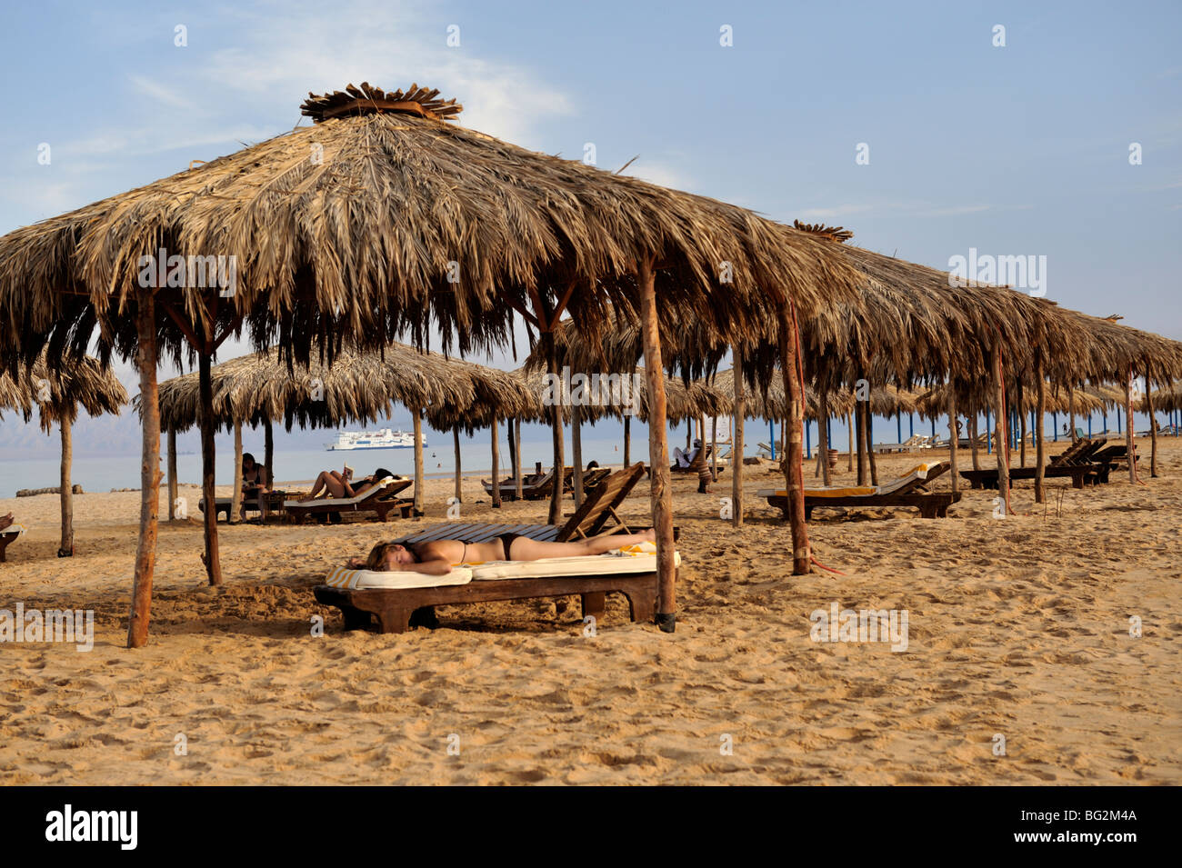 Sunbathing on tropical beach with thatched sunshades, Nuweiba, 'Red Sea', Sinai, Egypt Stock Photo