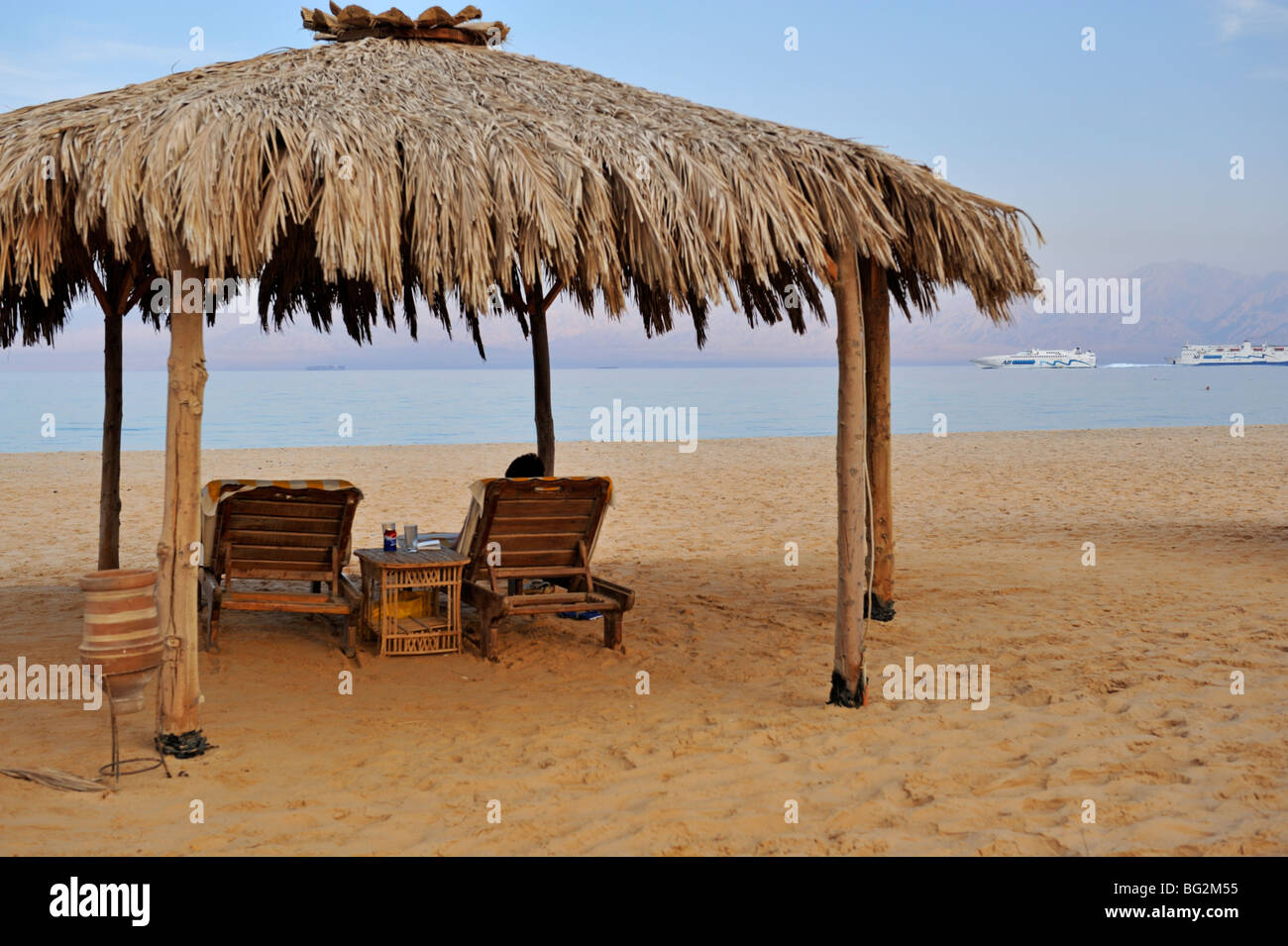 Relaxation on beach by sea under thatched sunshade, Nuweiba, 'Red Sea', Sinai, Egypt Stock Photo