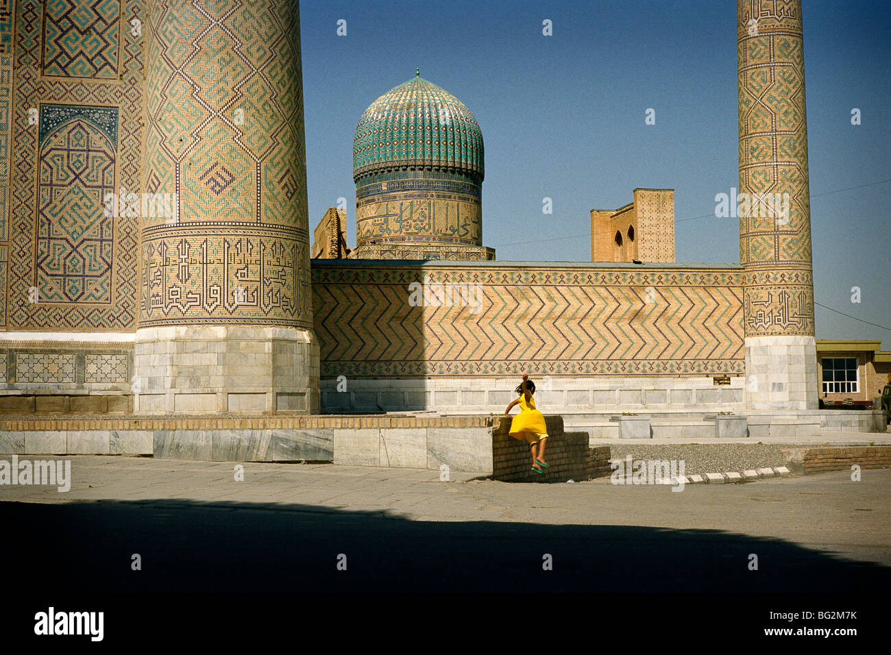 August 2008 - Samarkand, Uzbekistan. A yellow-dressed girl jump from the wall of the Bibi Khanoum mosque. Stock Photo