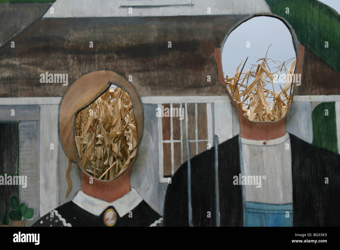 Painting of American Gothic with cut out faces, in front of corn field. Stock Photo