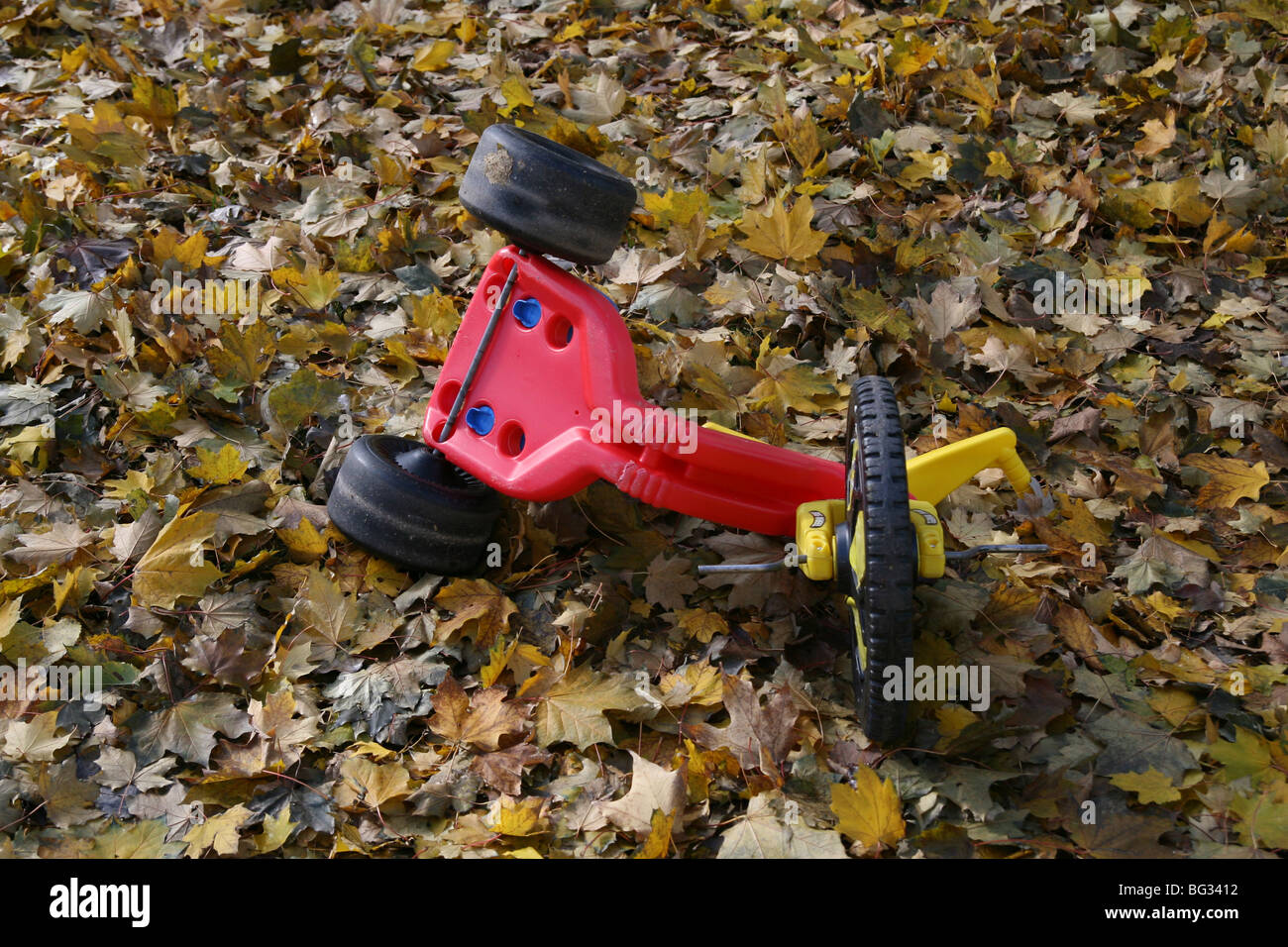 An over-turned tricycle in a pile of autumn leaves. Stock Photo