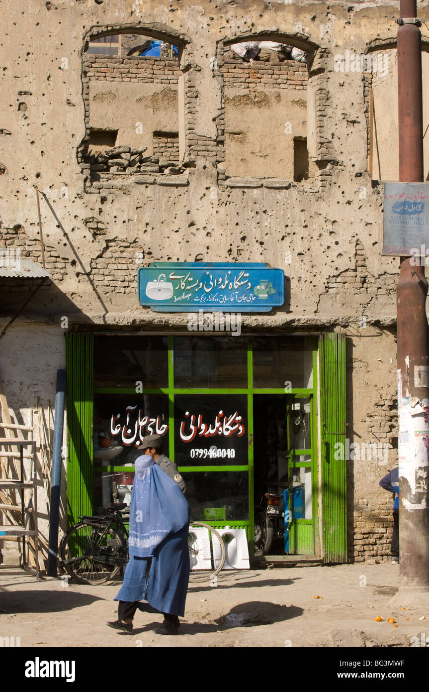 Afghan woman walks a bullet scarred shop in Kabul city, Afghanistan. Stock Photo