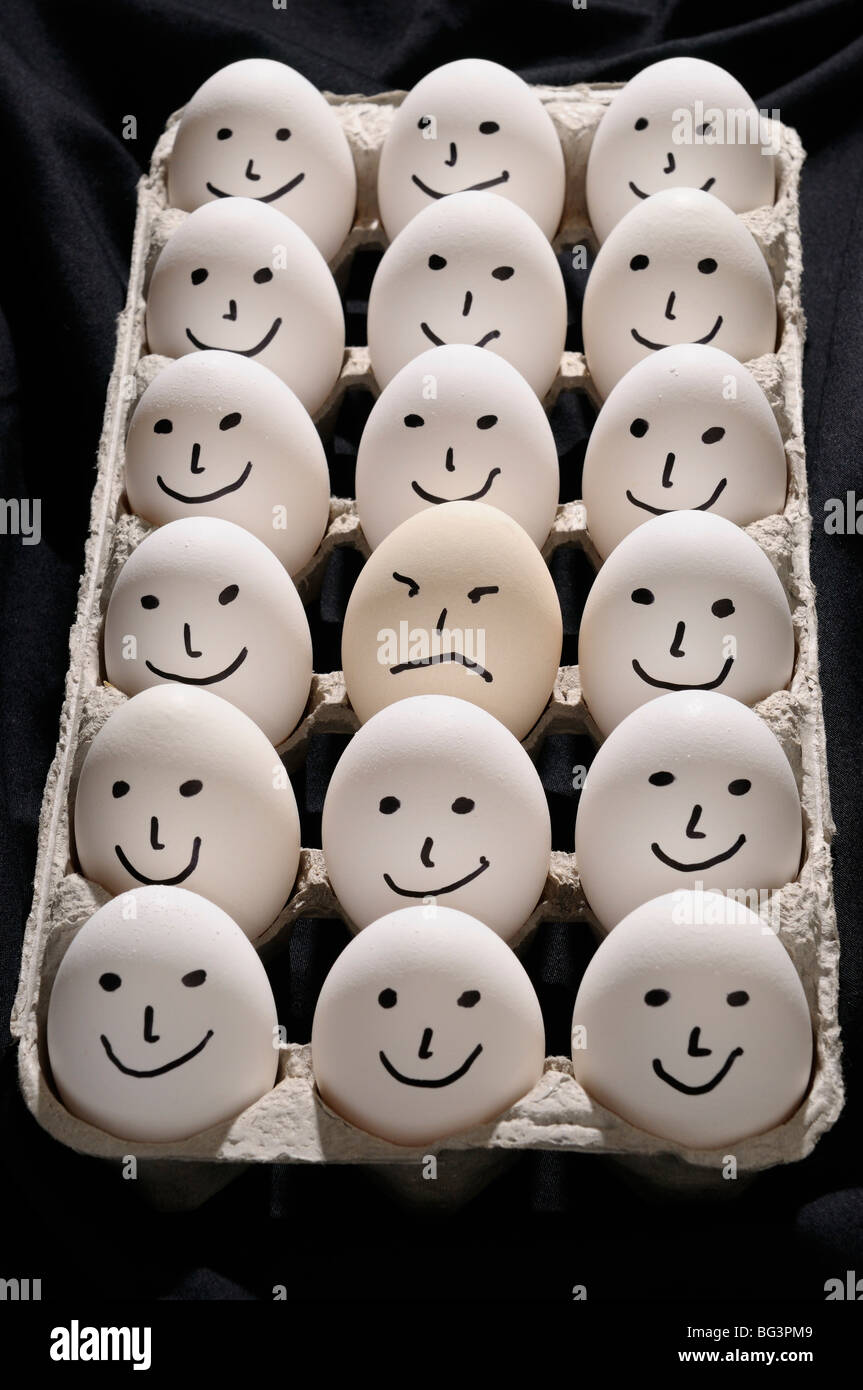 Package of backlit eggs on black cloth with smiling faces except for one grumpy sad face Stock Photo