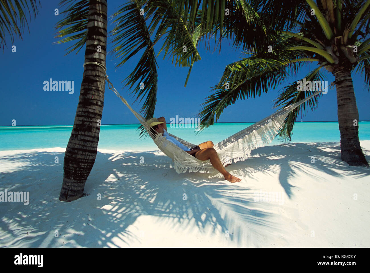 Man relaxing on a beachside hammock, Maldives, Indian Ocean, Asia Stock Photo