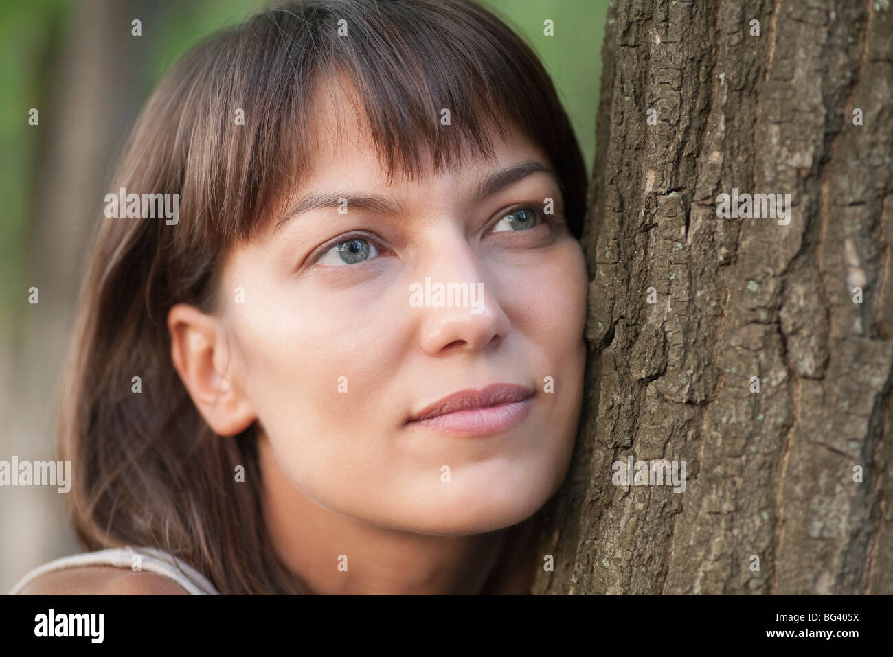 Woman leans on tree trunk with a faraway look in her eyes Stock Photo