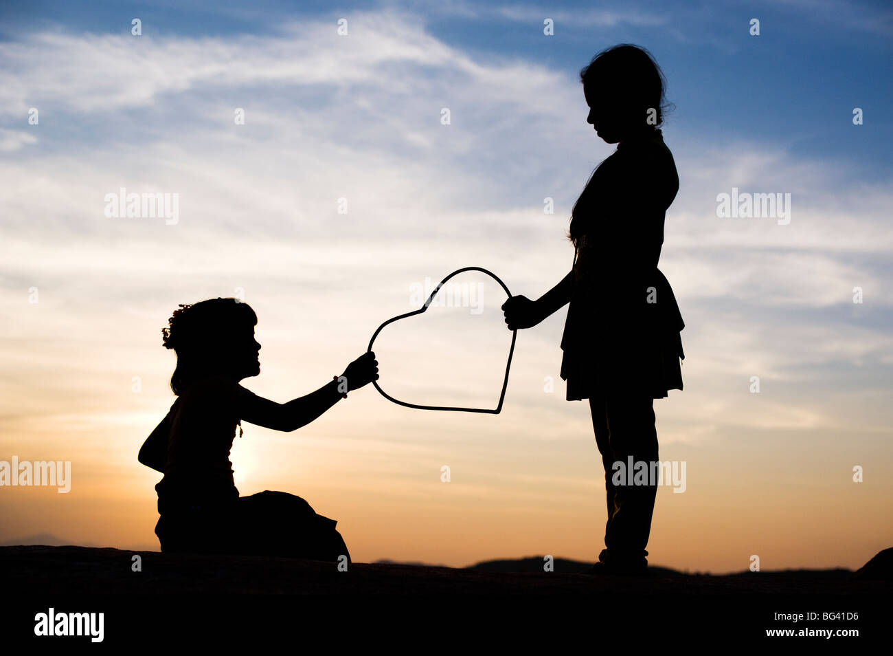 Silhouette of a two young Indian girls giving and taking a heart shape at sunset. India Stock Photo
