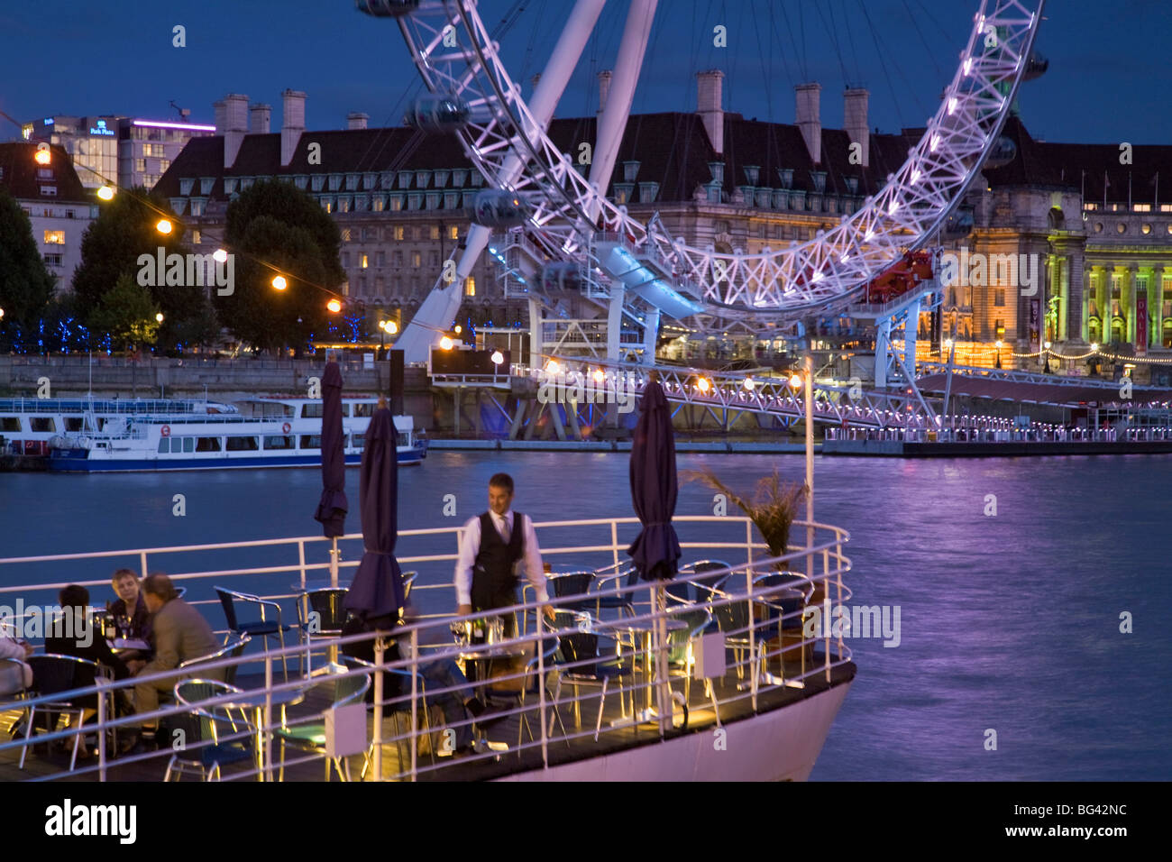 England, London, Westminster, People having drink on the deck of The Hispaniola restaurant boat, with the London Eye Stock Photo