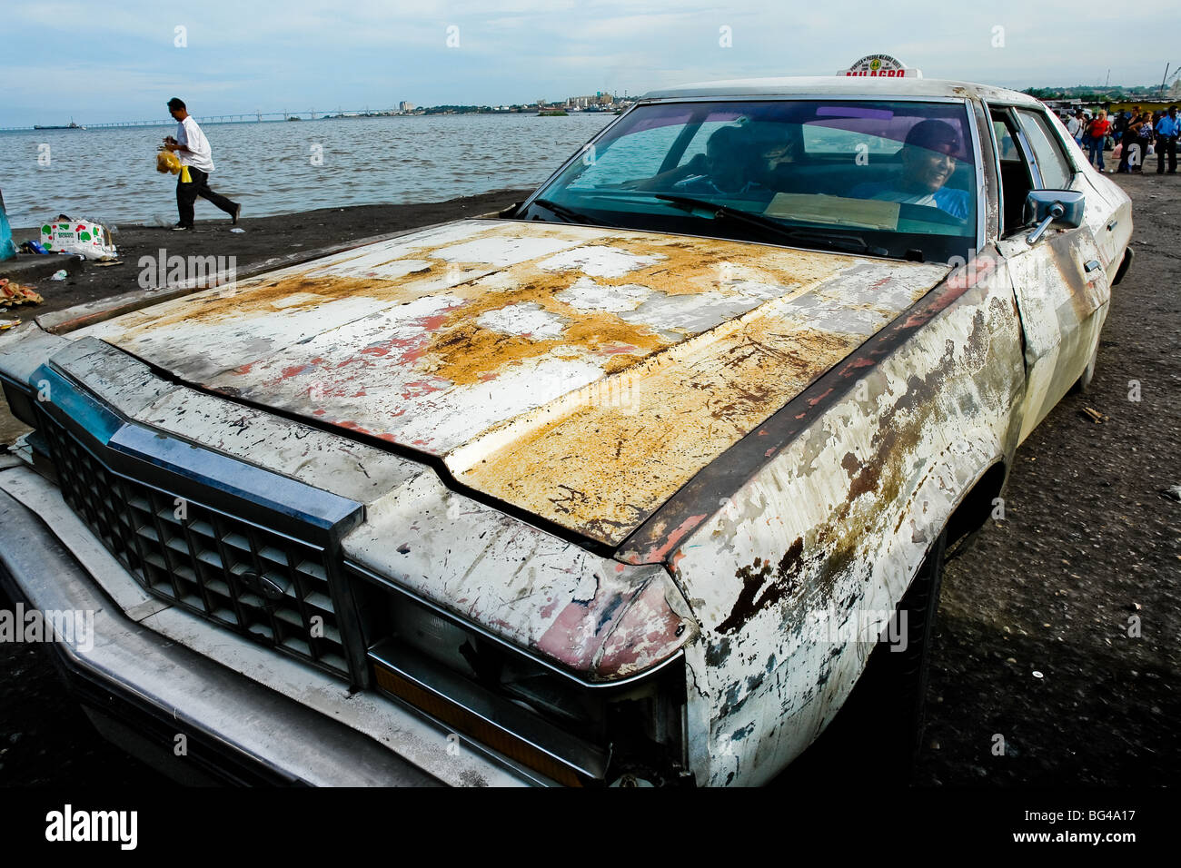 A rusty American classic car from 1970s, used as a shared taxi, parked on the bank of the lake Maracaibo, Venezuela. Stock Photo