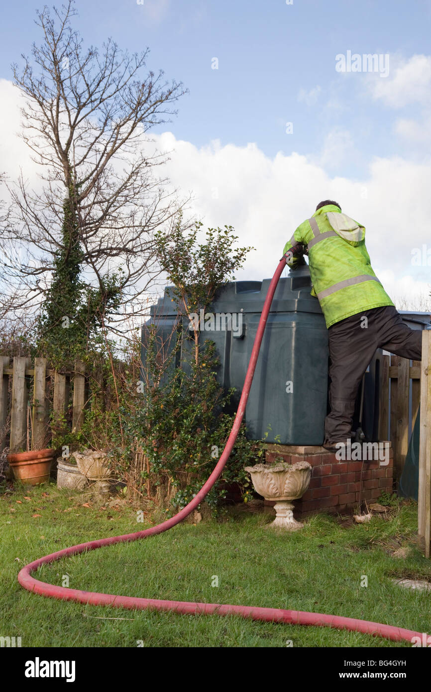 Man filling a domestic oil tank with supply pipe across the lawn. Wales, Britain, UK. Stock Photo