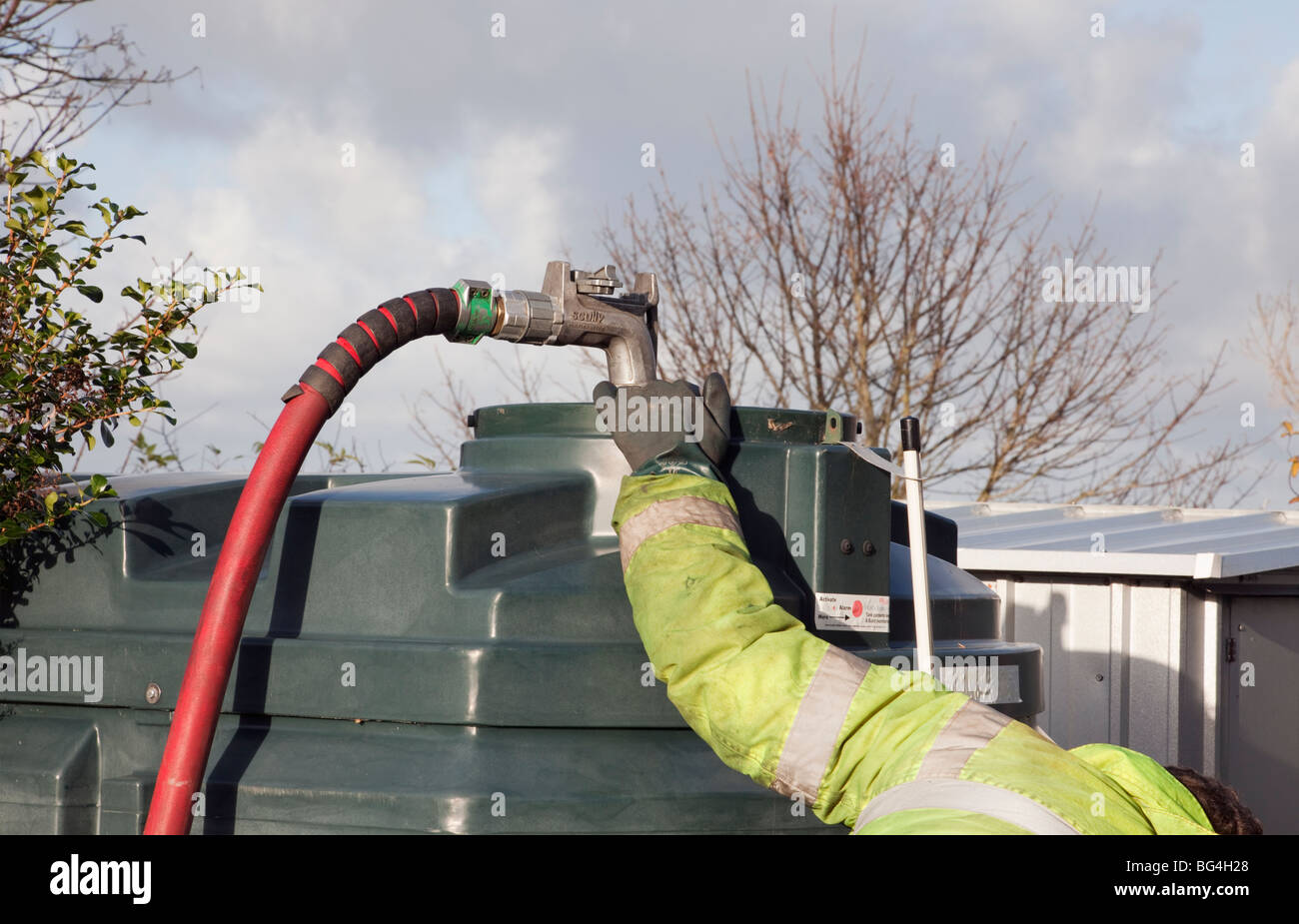 Man filling a domestic oil tank with red supply pipe and nozzle. Britain, UK, Europe Stock Photo