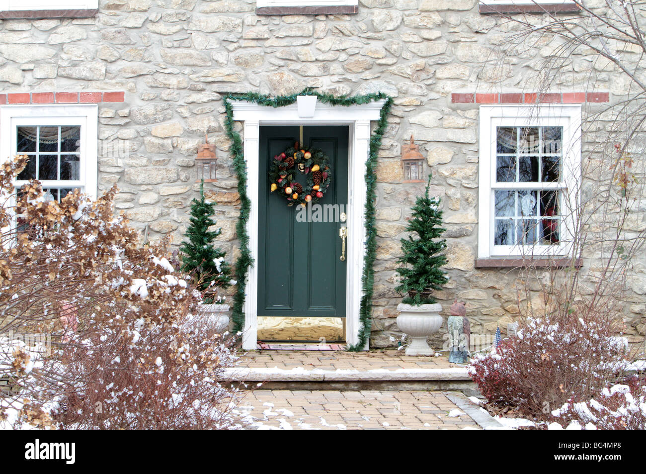 A beautiful shot of a vintage historic stone house decorated for Christmas. A wreath a green front door evergreens and garland. Stock Photo