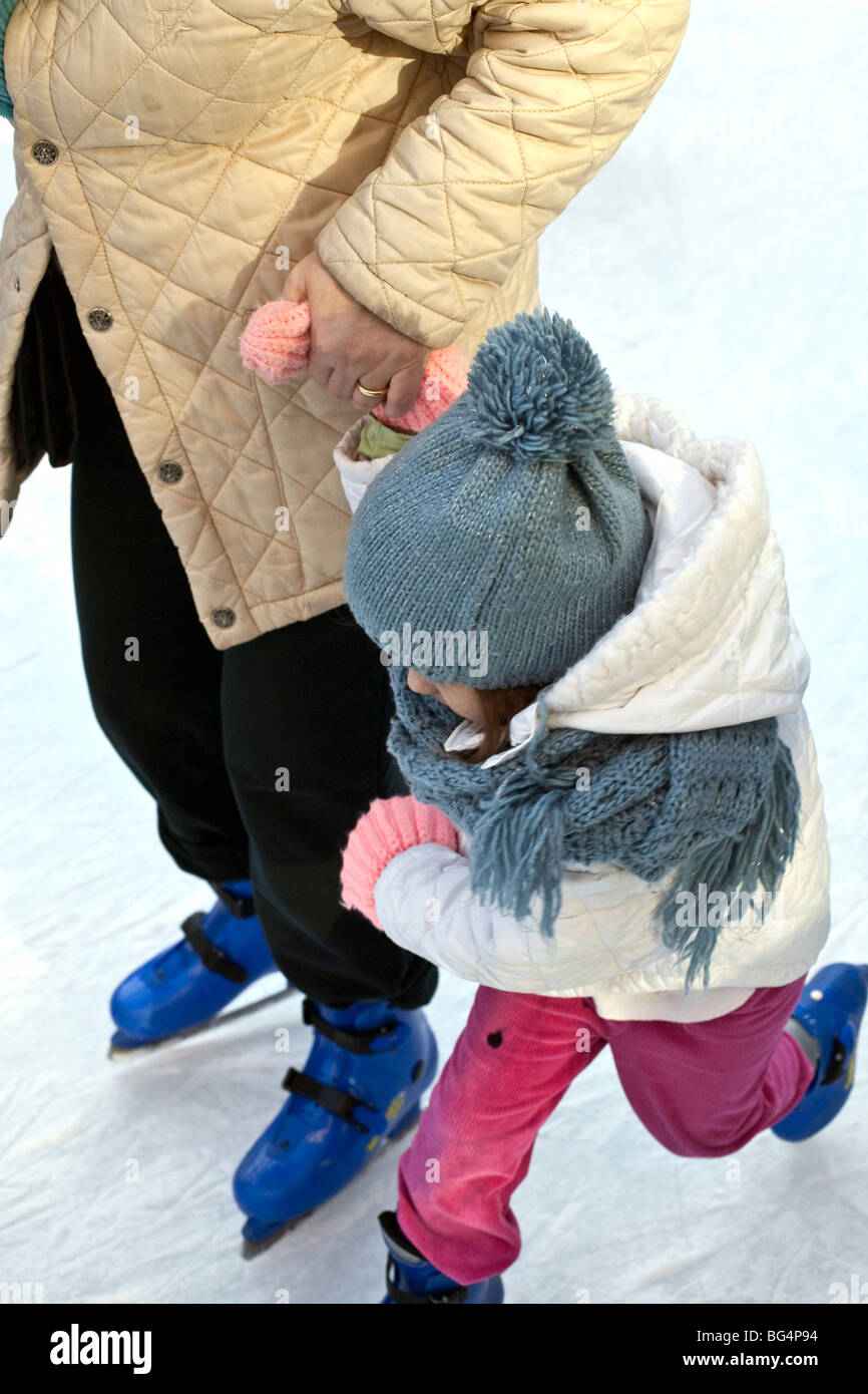 tiny girl dynamo on skates wearing blue pompom hat & holding her mom's hand  makes determined effort to keep up the pace on ice Stock Photo - Alamy
