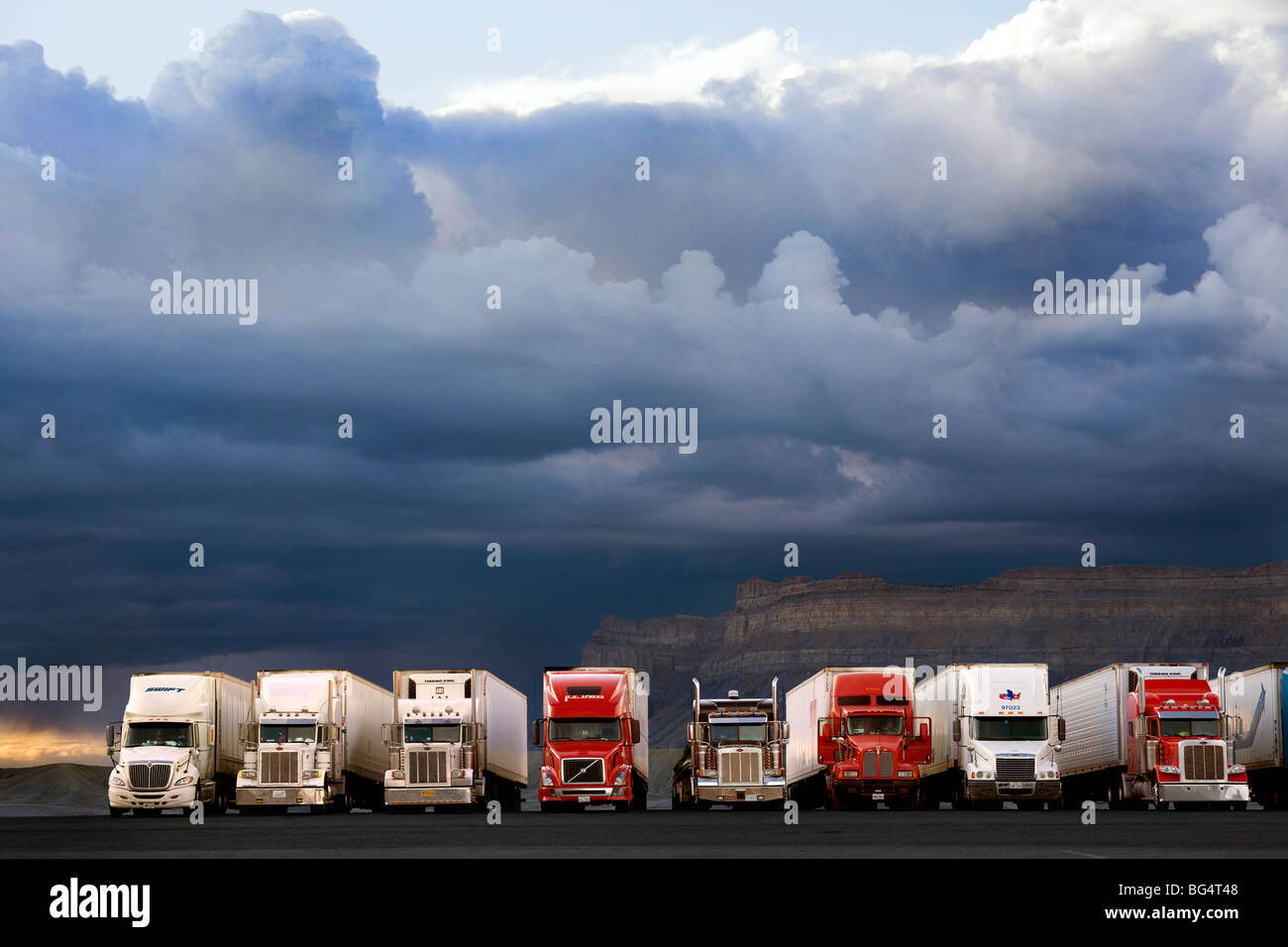 Row of American trucks at  the Green River Utah truckstop with dark clouds of a rain and thunderstorm over the mountains. US USA Stock Photo