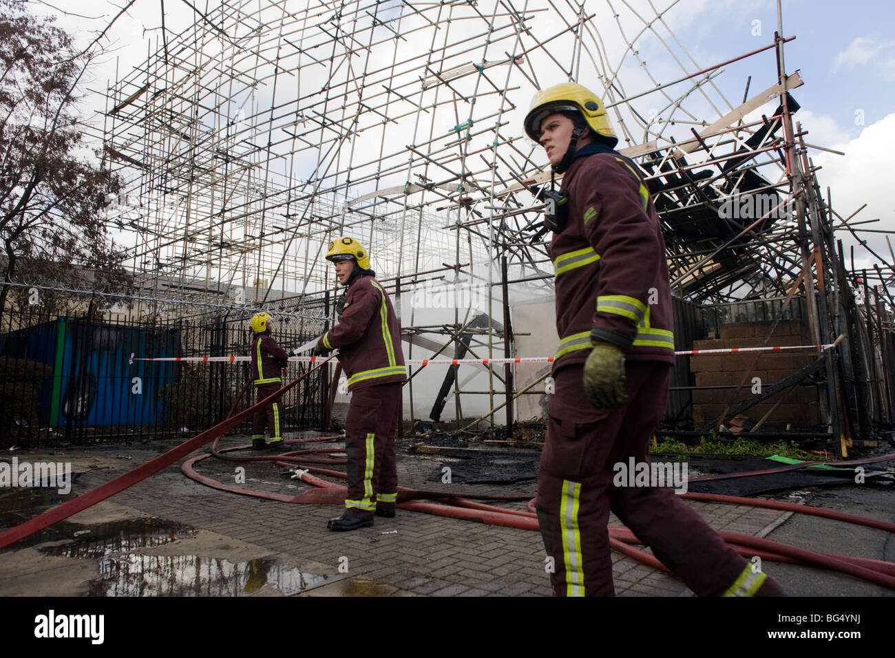 Three London Fire Brigade fire fighters attend to smouldering remains after an inner-city estate fire in south London. Stock Photo