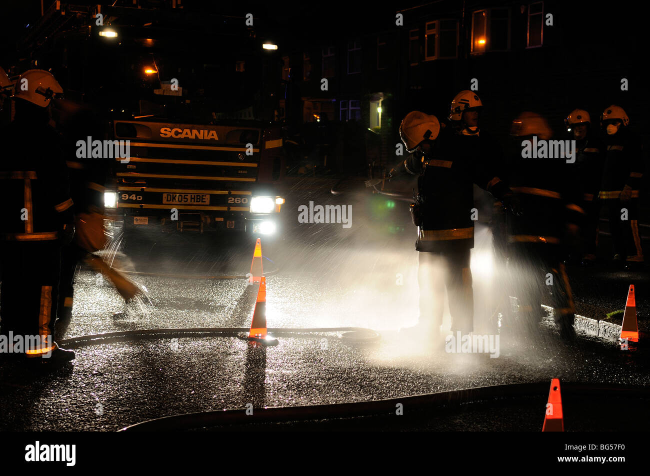 Firemen being decontaminated at night with hosereel jet Stock Photo