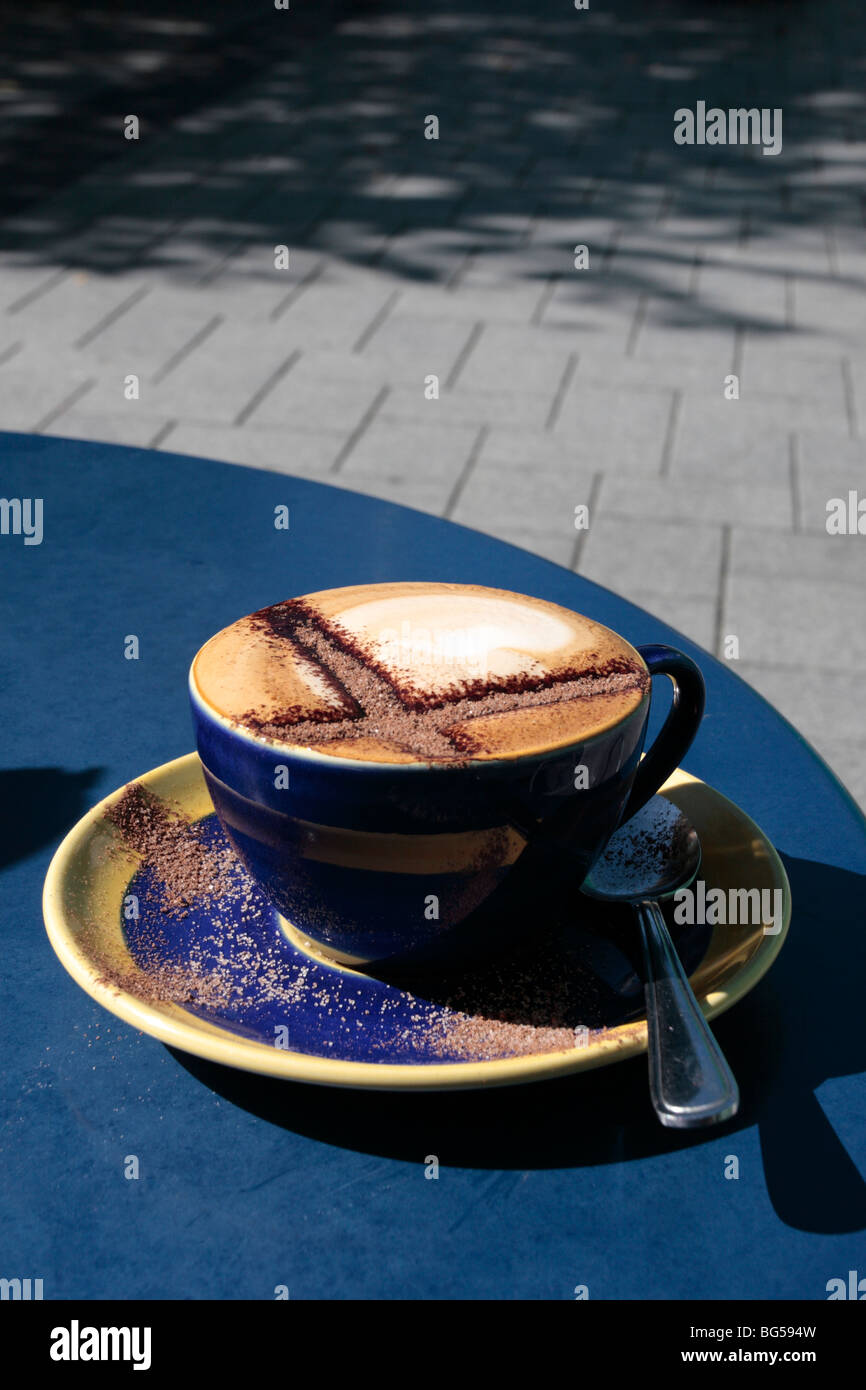 Cappuccino with a chocolate cross on top in a blue cup and saucer on a blue table Stock Photo