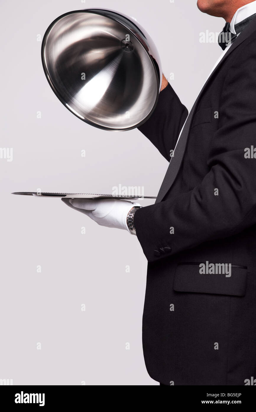 Butler lifting the cloche from a silver serving tray, insert your own object onto the tray. Stock Photo