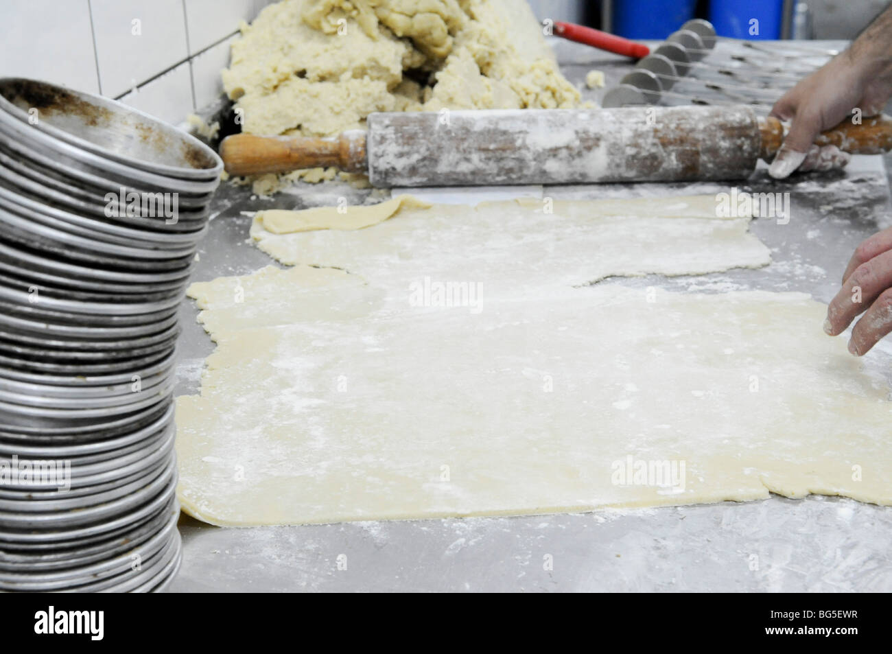 Industrial Bakery. Baker kneading and flattening dough Stock Photo