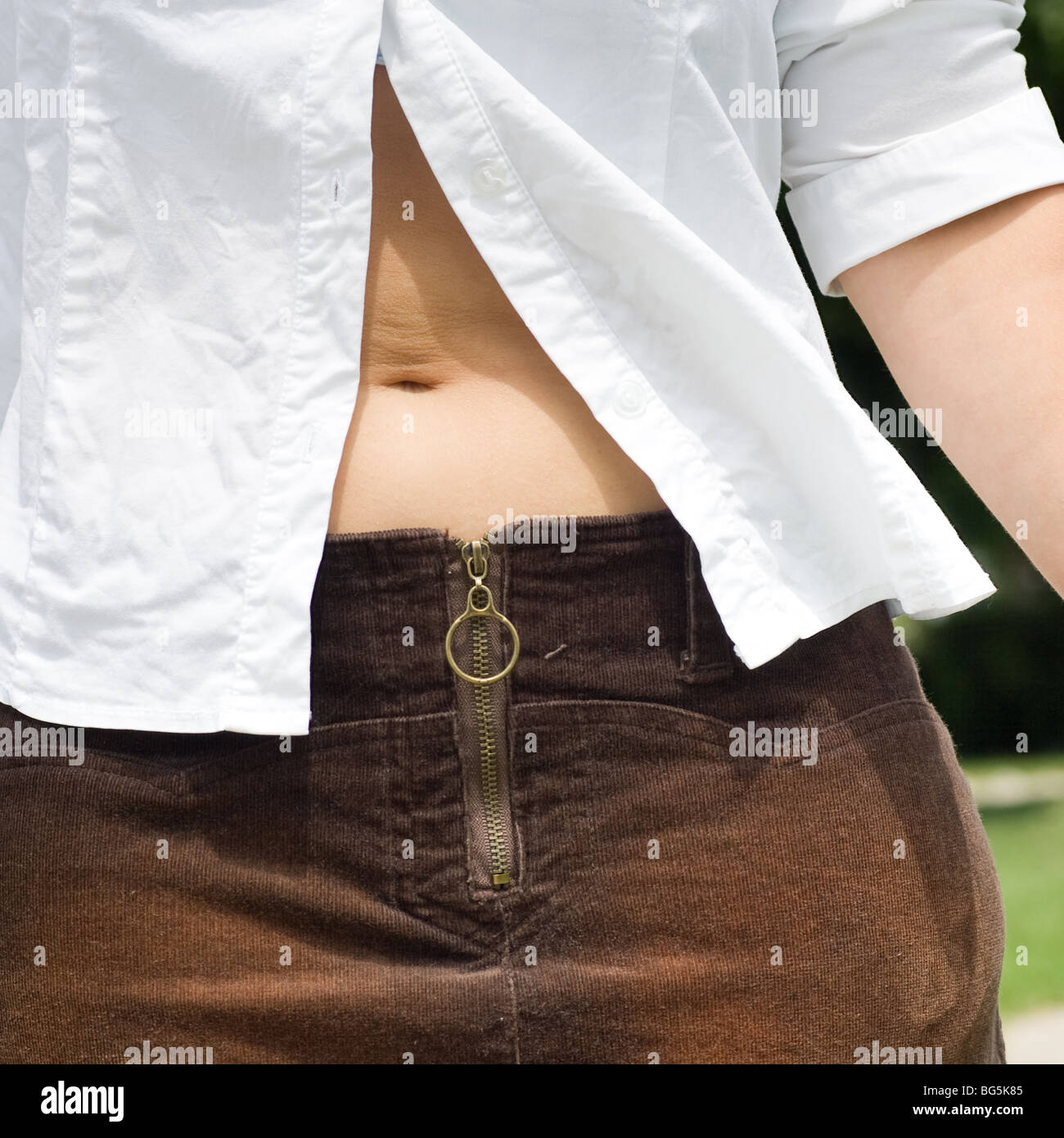 Closeup of a woman's mid-section, revealed by an unbuttoned white shirt, showing the belly button. Stock Photo