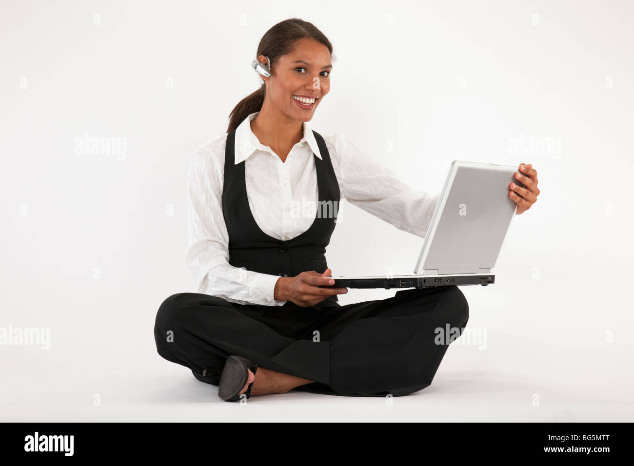 Young woman sitting on floor using laptop and wearing blue tooth headset. Horizontally format. Stock Photo