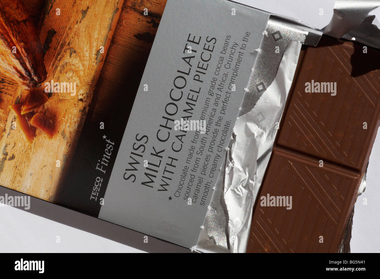 partly unwrapped bar of Tesco Finest Swiss Milk chocolate with caramel pieces Stock Photo