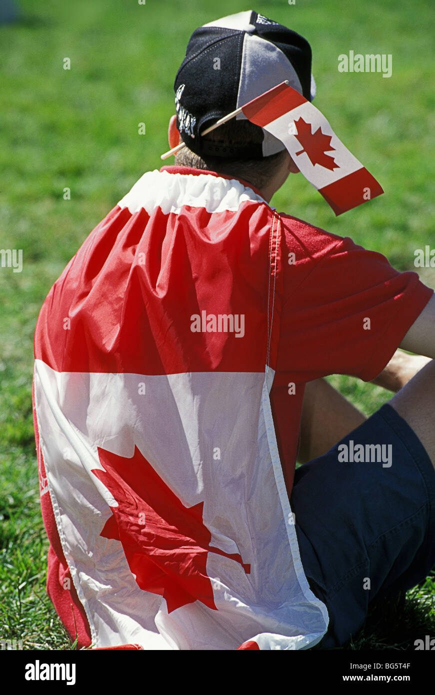 Patriotic Man wrapped with Canadian Flag sitting on lawn of Parliament Hill celebrating on Canada Day, Ottawa, Ontario, Canada Stock Photo
