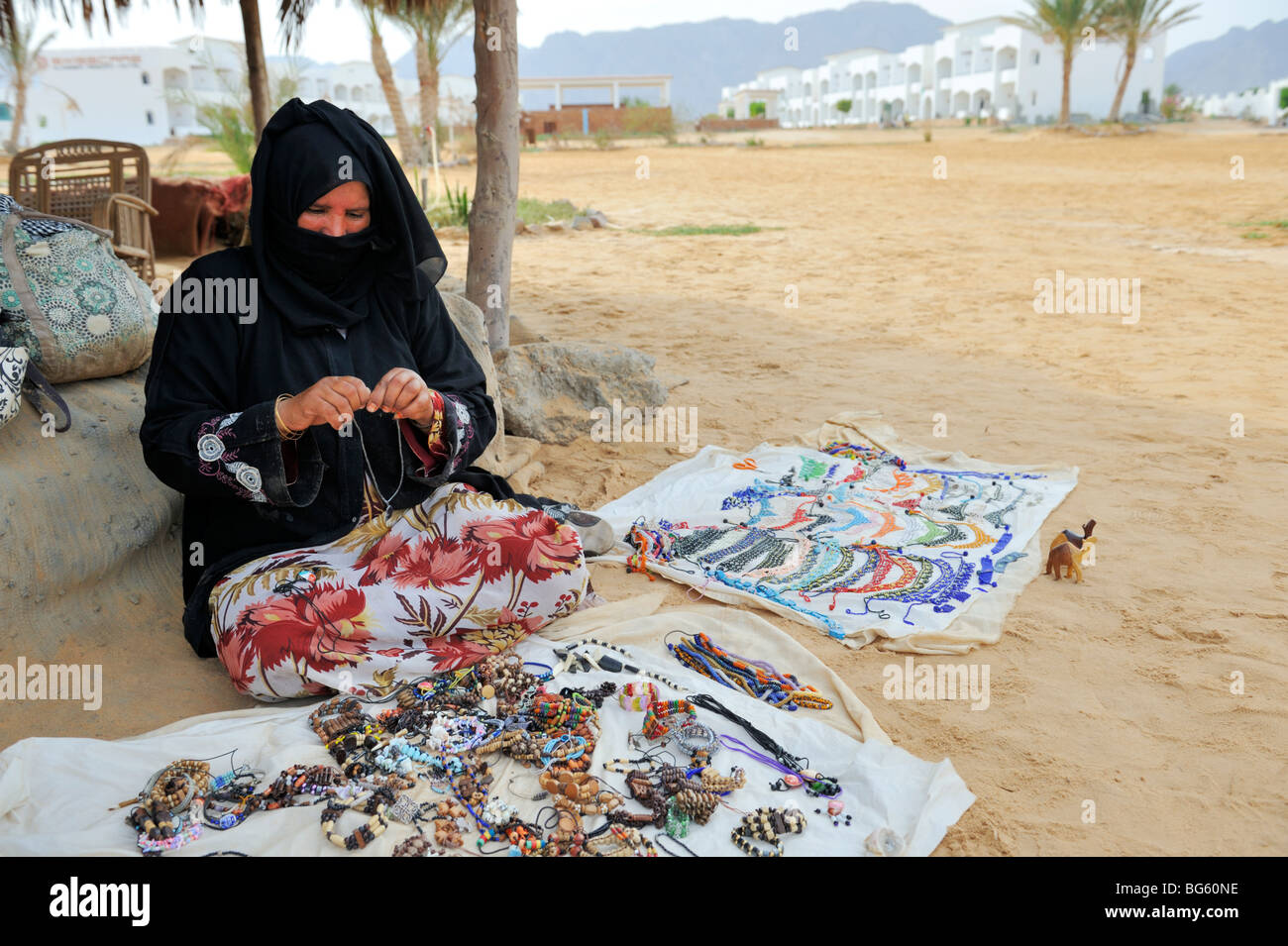 Bedouin woman sitting on traditional carpet selling trinkets and jewellery, Nuweiba beach, Sinai, Egypt Stock Photo