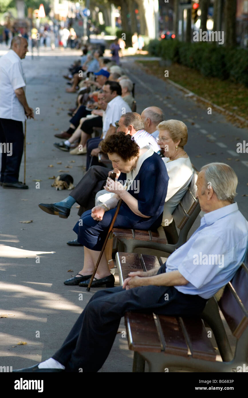 Old people take it easy and eat snacks during siesta on park benches in a city park near Sagrada Familia Barcelona Catalonia Spain Stock Photo