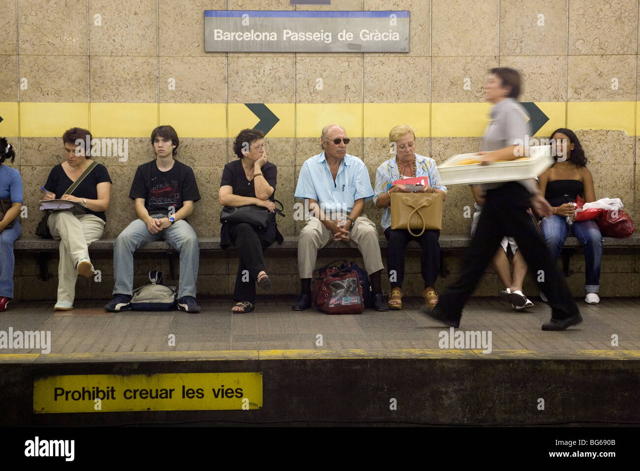 A delivery worker passes passengers on underground platform Passeig de Gracia Barcelona Catalonia Spain Stock Photo