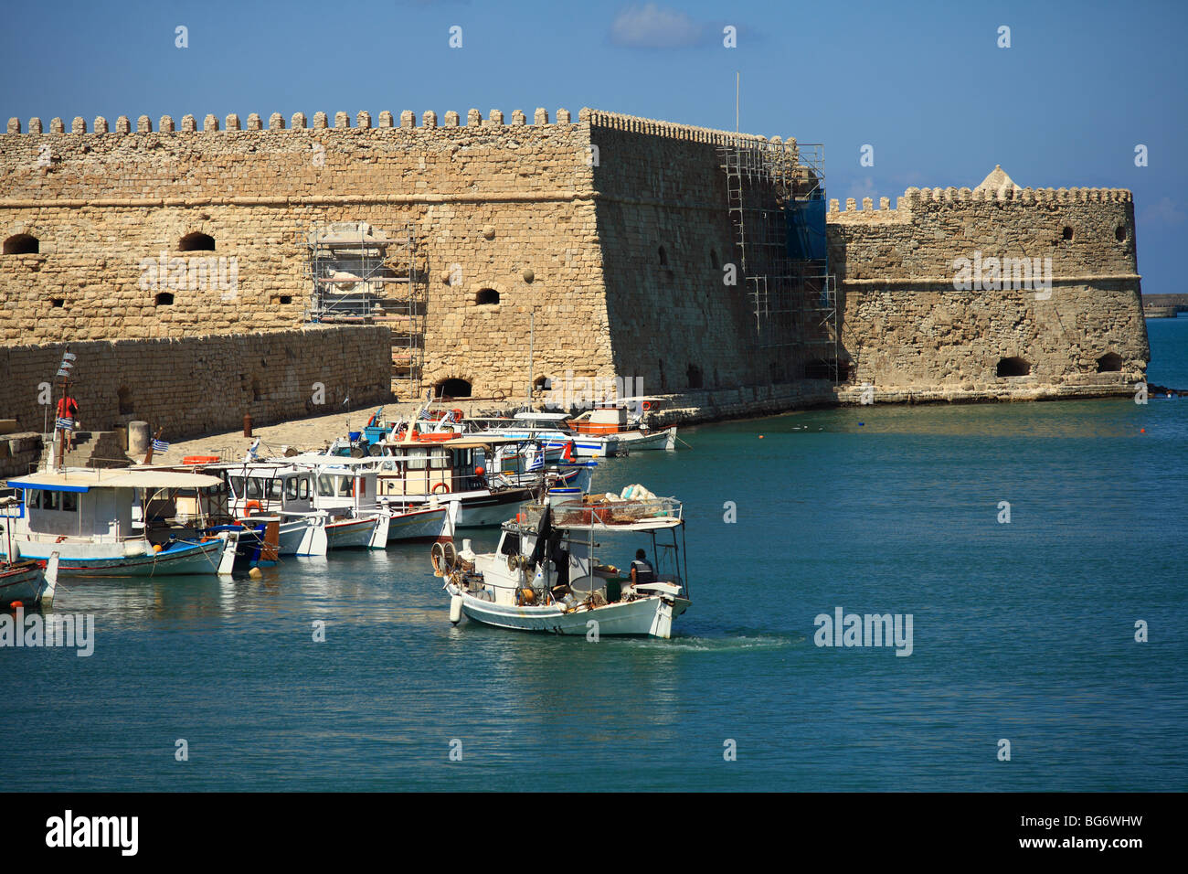 A caique sets off from Heraklion fishing harbour for an evening's fishing, with the Venetian era Koule fortress behind Stock Photo
